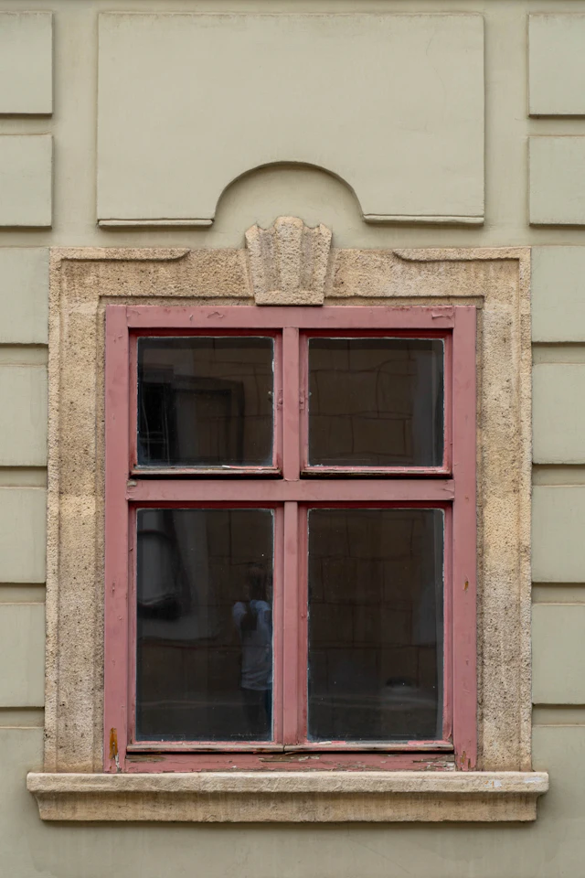 A rectangular window with a faded red frame set in a stone wall