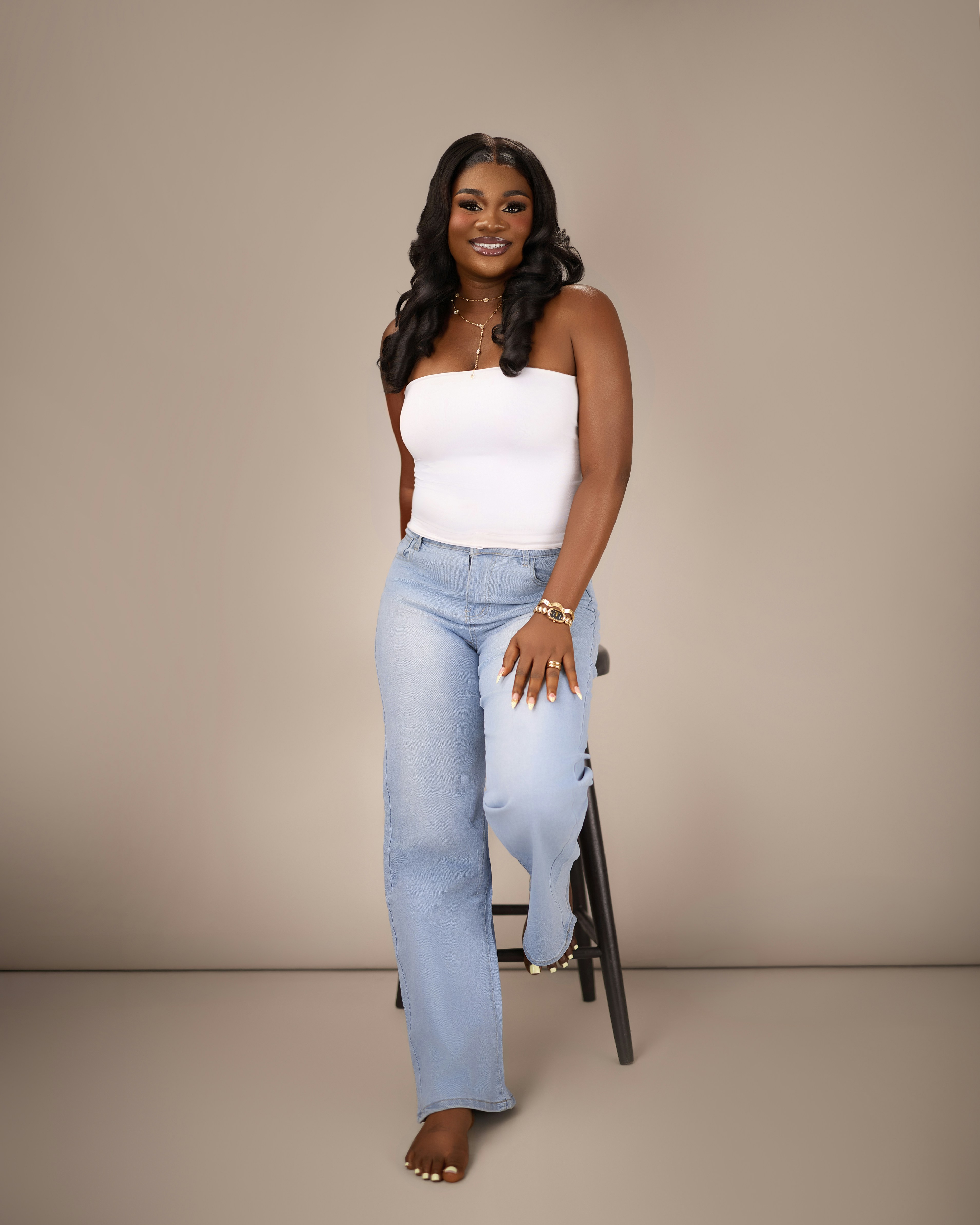 A woman in a white tube top and light blue jeans on a stool
