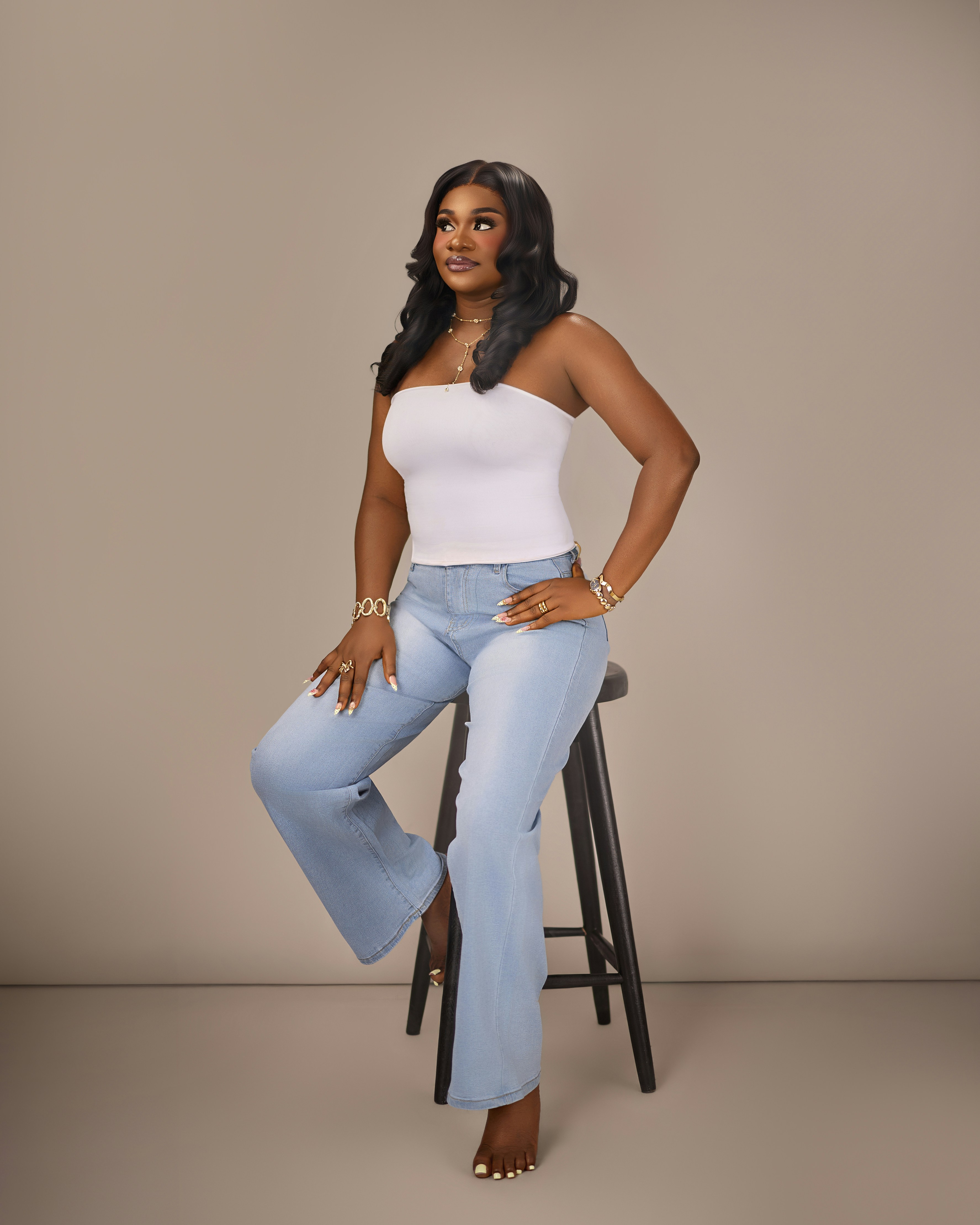 A woman in a white tube top and light blue jeans on a stool