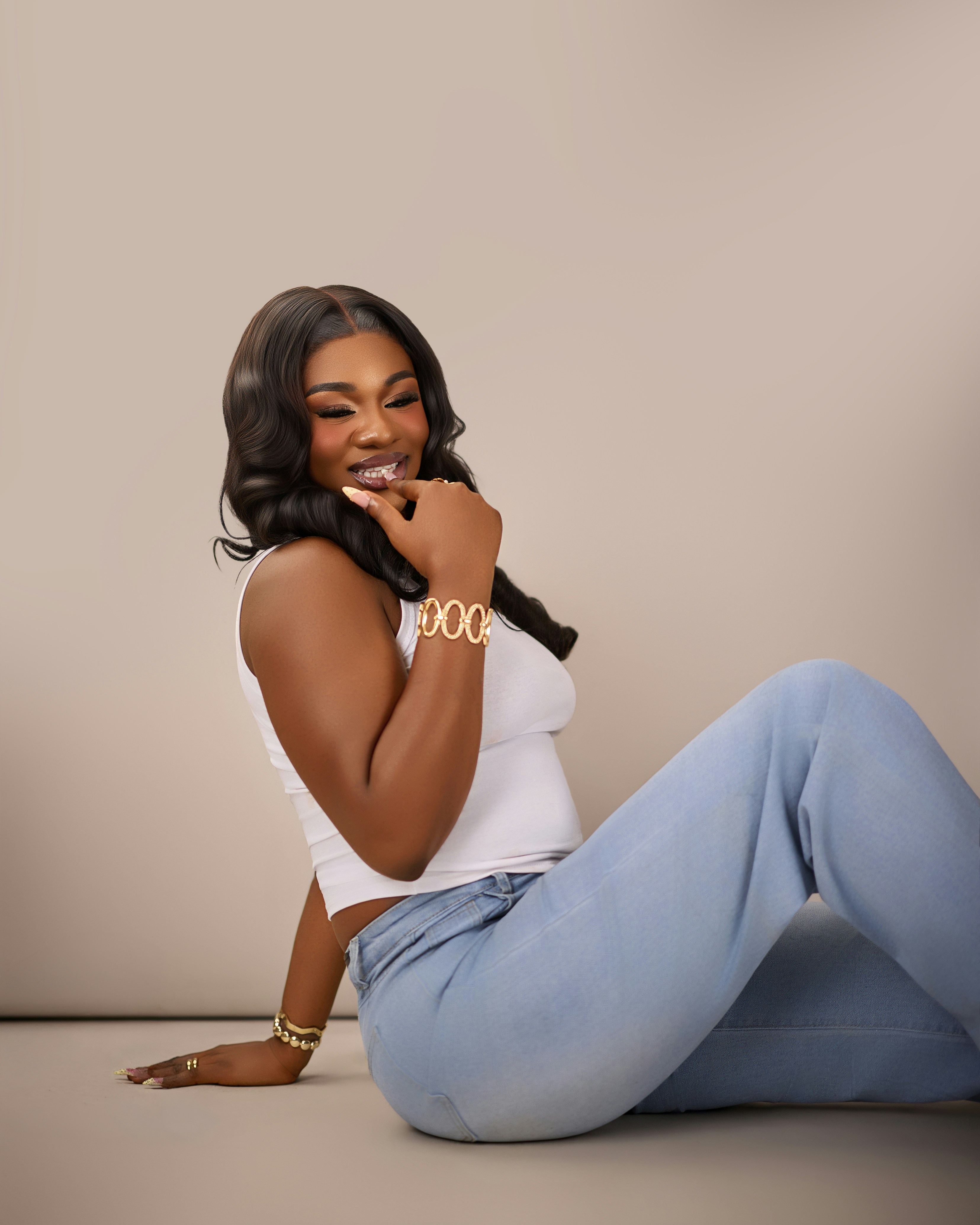 A woman in a white tank top and light blue jeans sitting on the floor