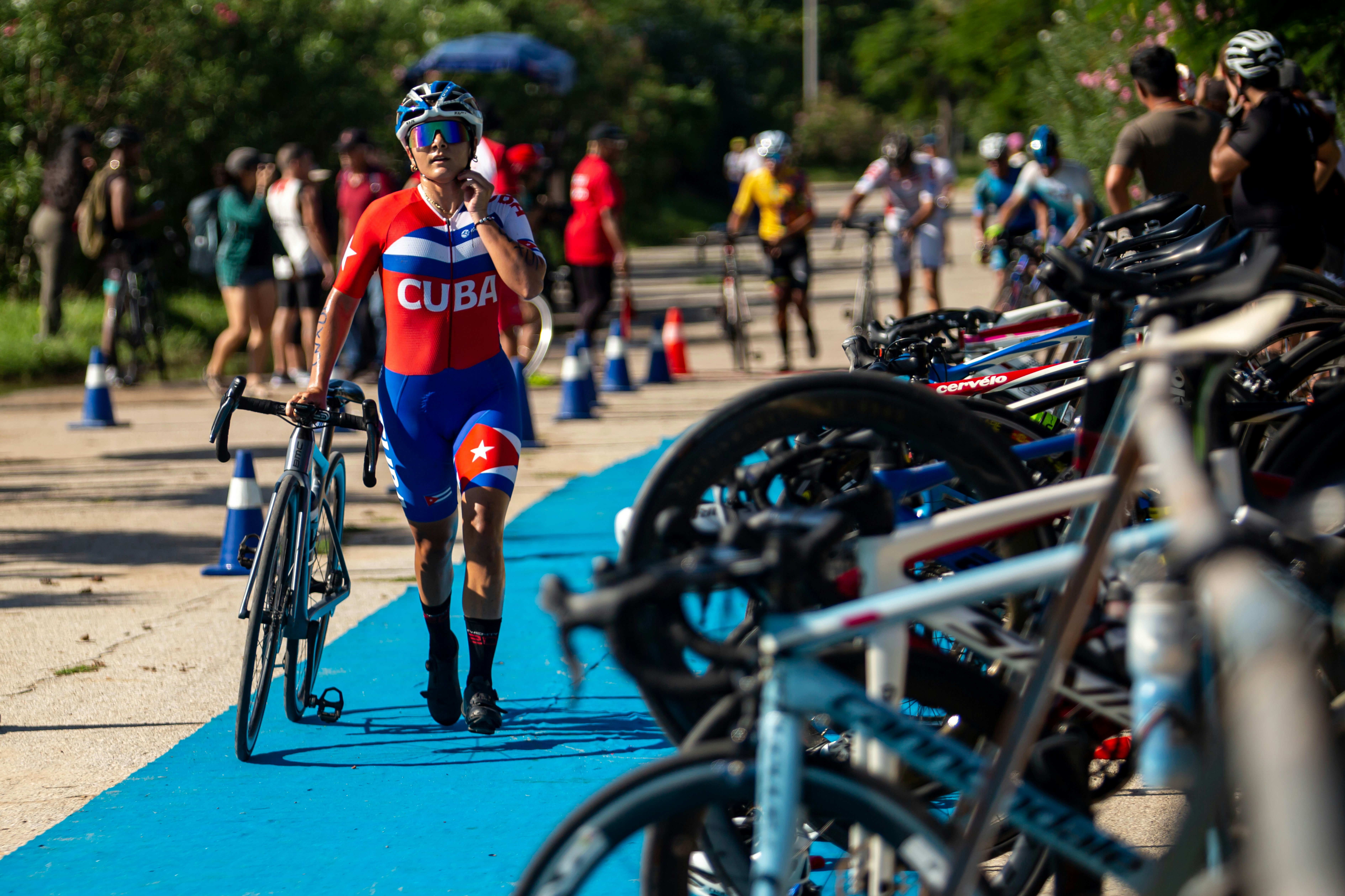 A cyclist in a red and blue Cuba jersey walking with a bicycle