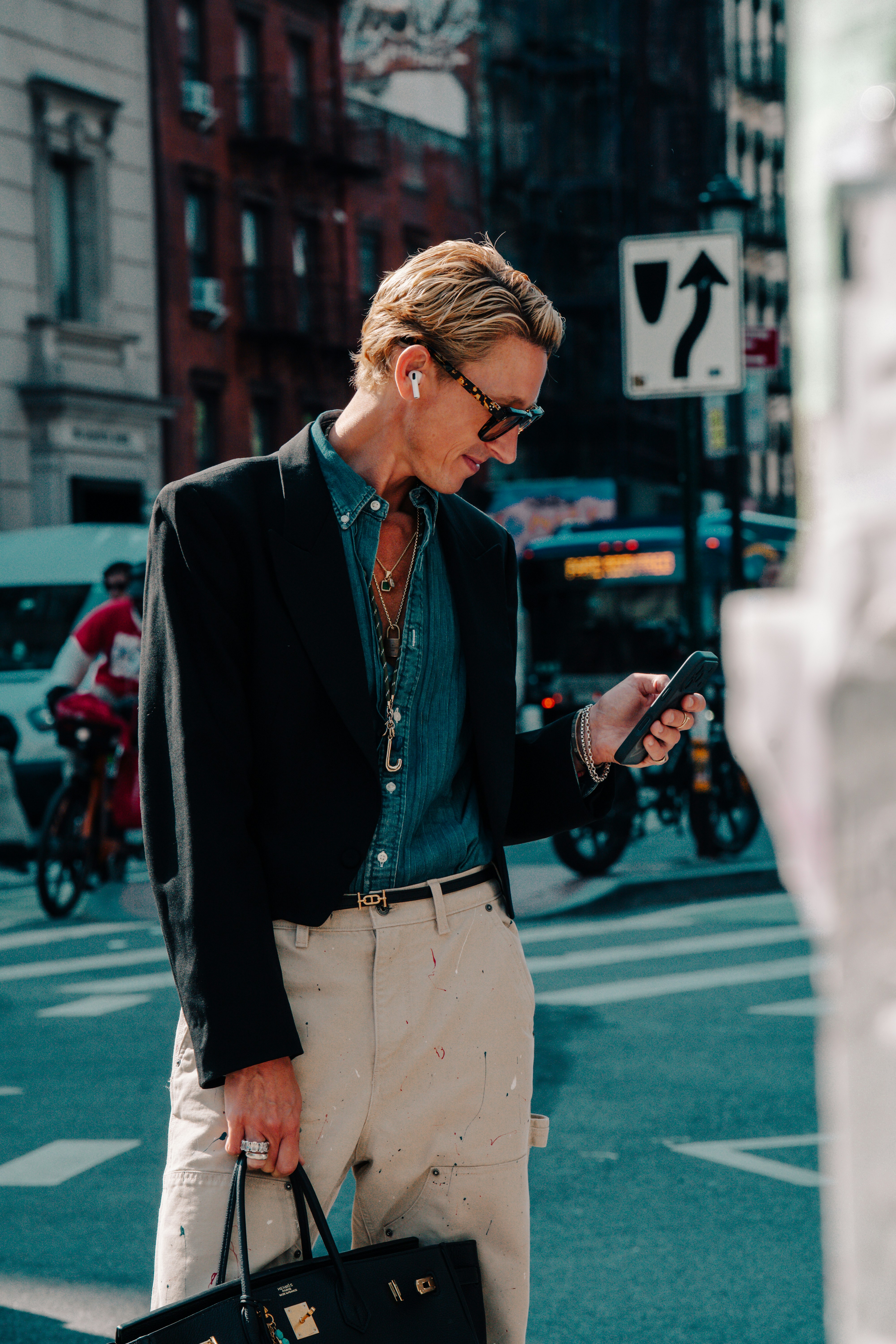 A person in a black blazer and denim shirt using a smartphone on a street