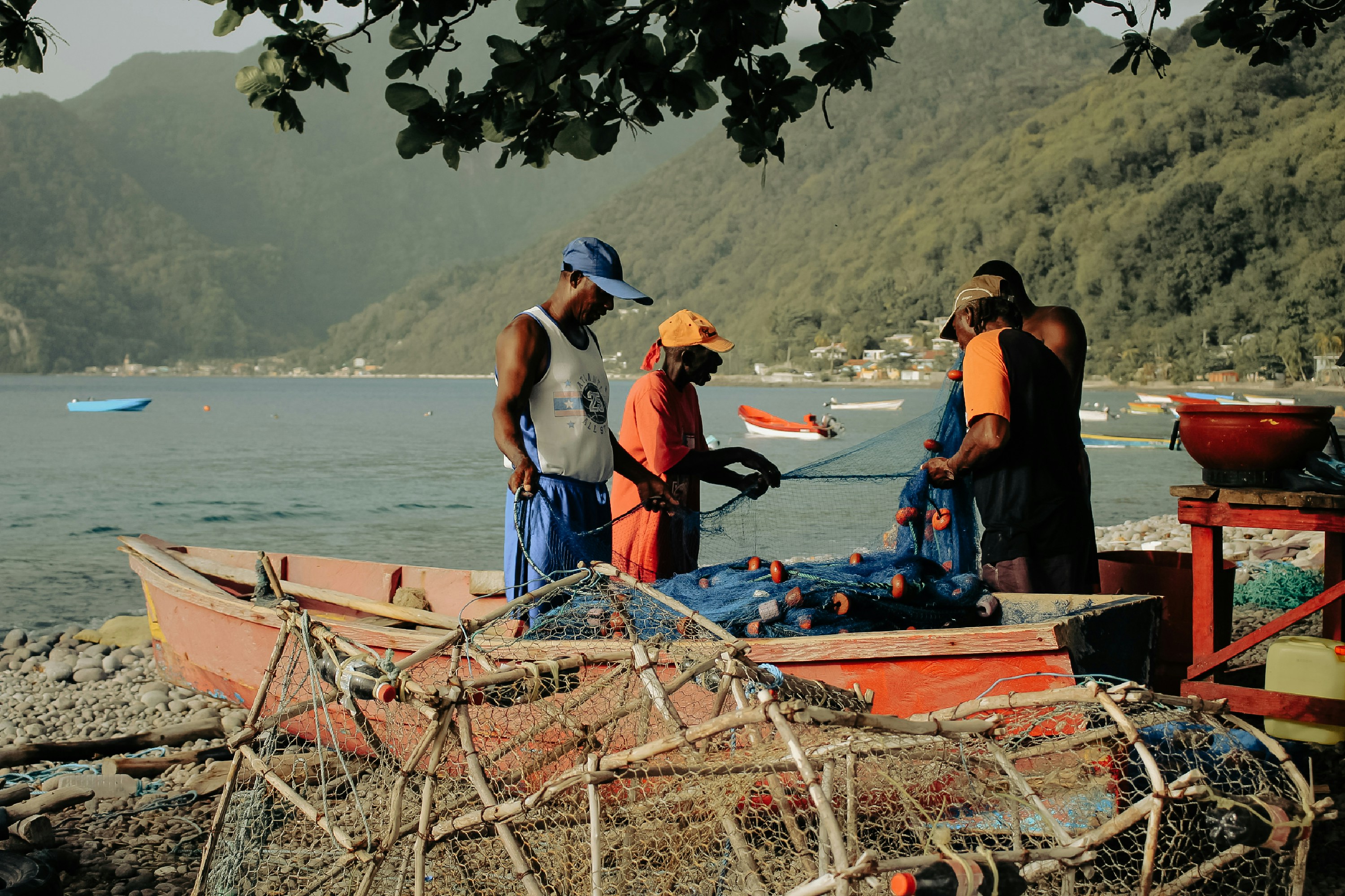 Tre uomini che lavorano con reti da pesca blu su una barca di legno su una spiaggia