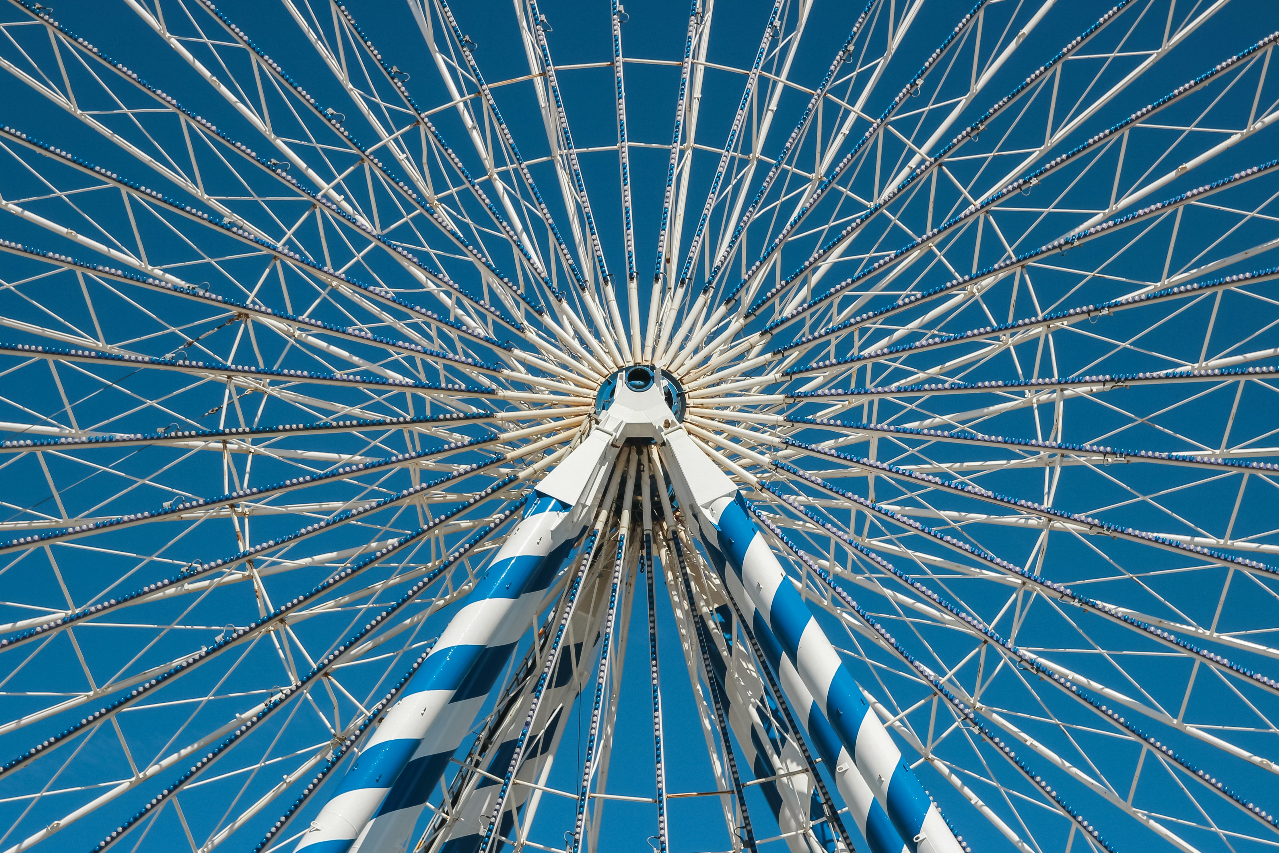 The white and blue metal spokes of a large ferris wheel against blue sky