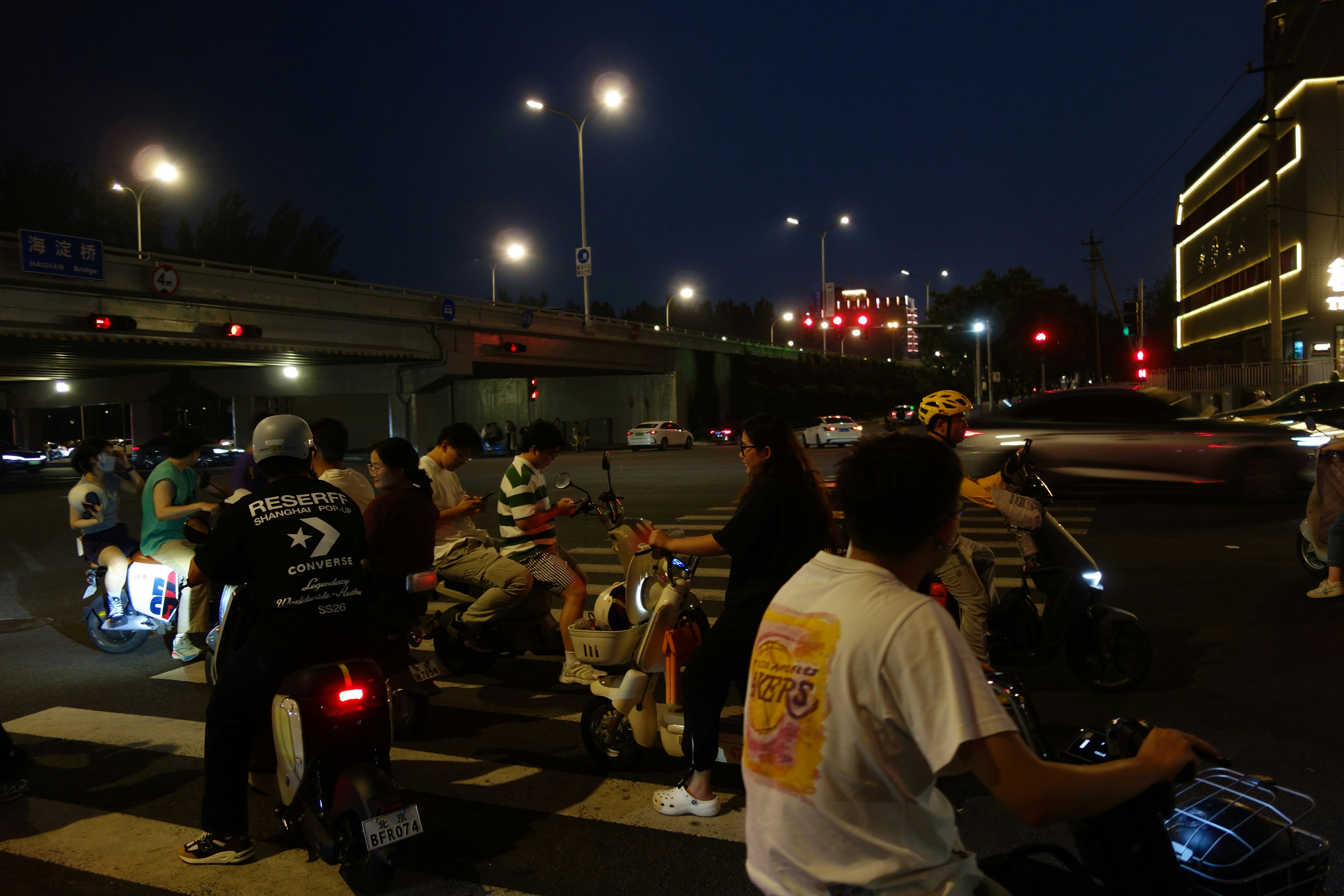 People on electric scooters waiting at a night intersection under streetlights