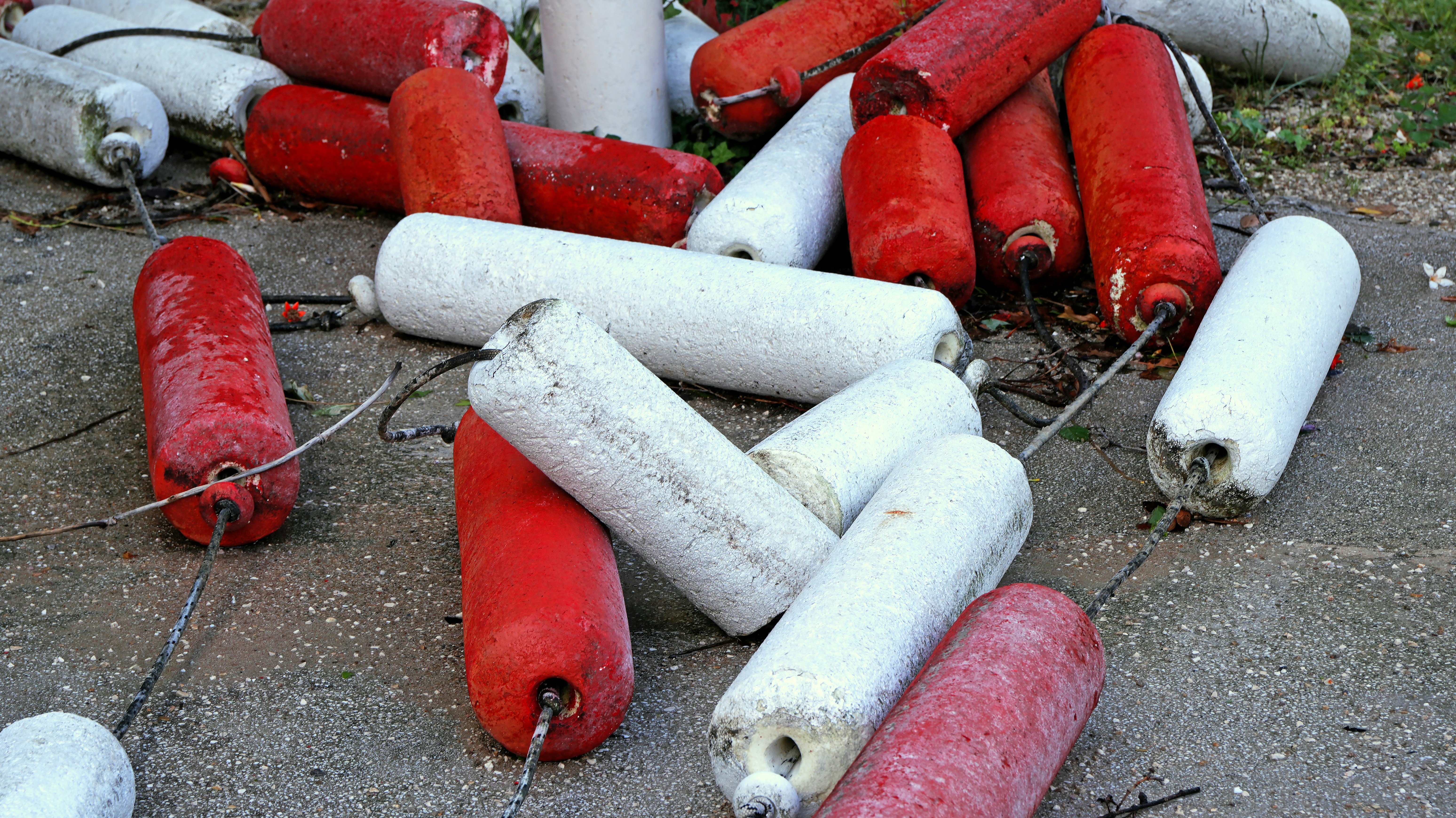 Red and white cylindrical foam boat fenders scattered on a grey concrete surface