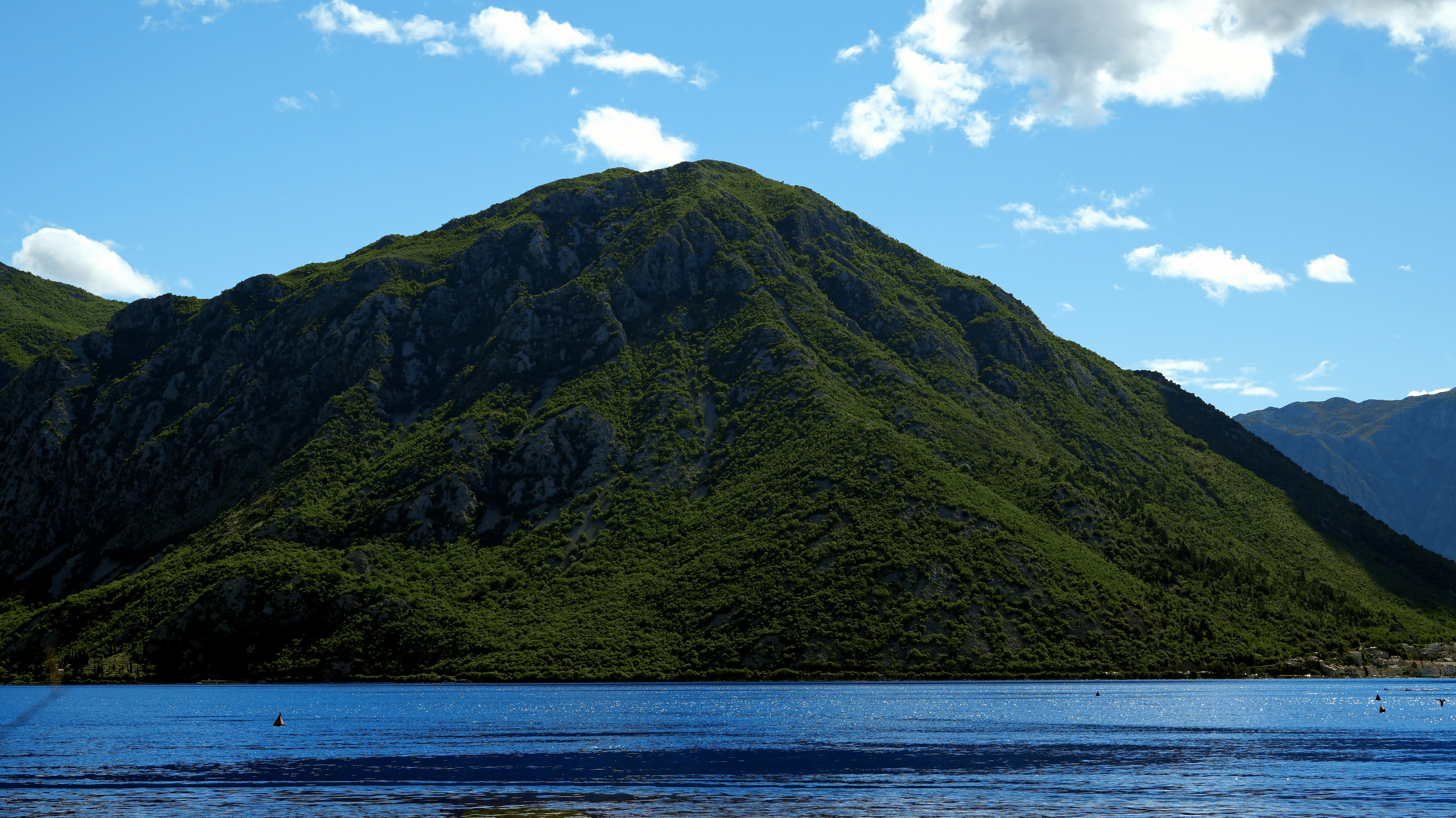 A large green mountain rising above a deep blue bay under a sunny sky
