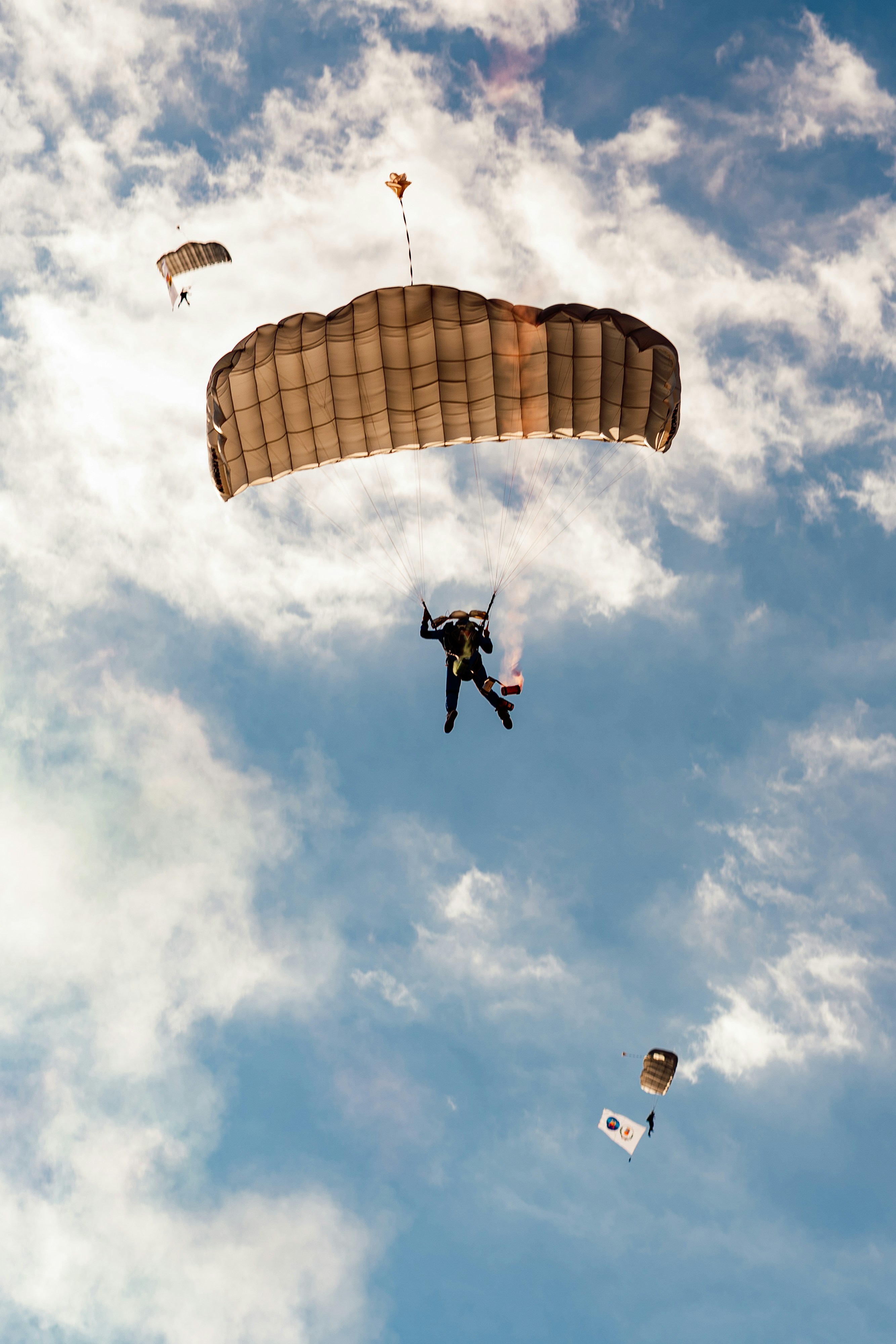A skydiver with a parachute and a smoke flare against a cloudy sky