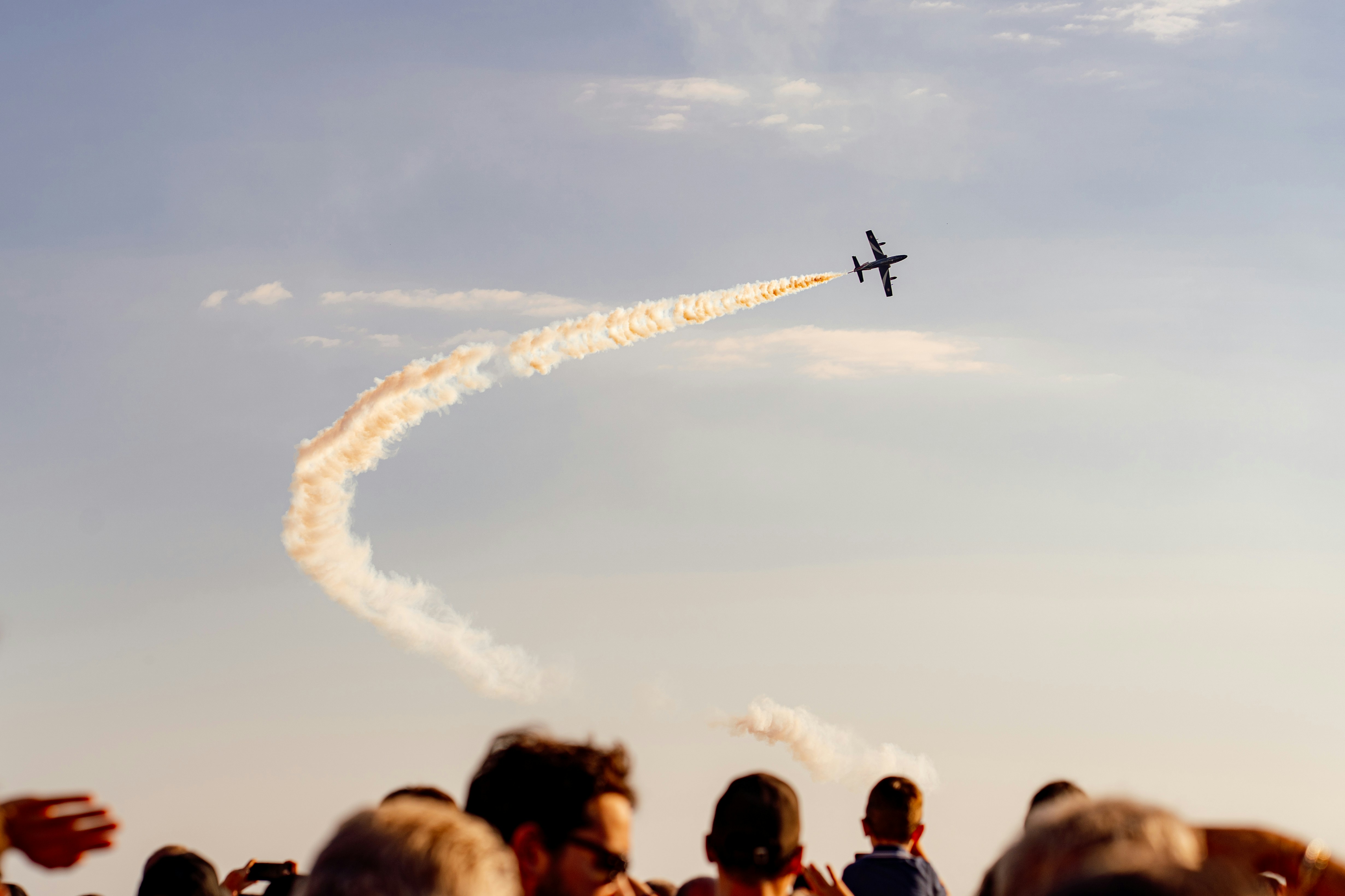 A jet plane leaving a curved white smoke trail above a crowd of people