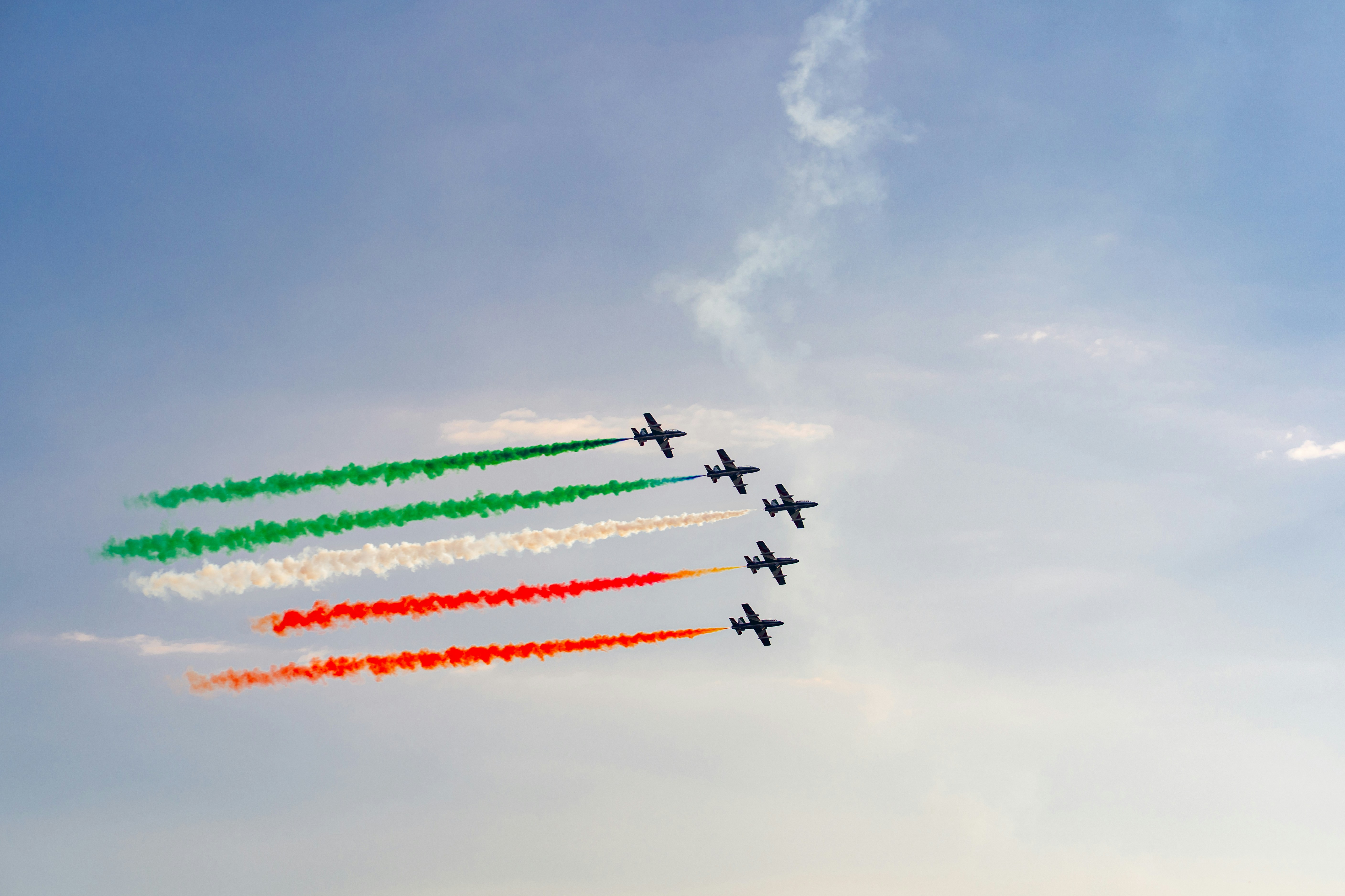 Five fighter jets flying in formation leaving green, white, and red smoke trails