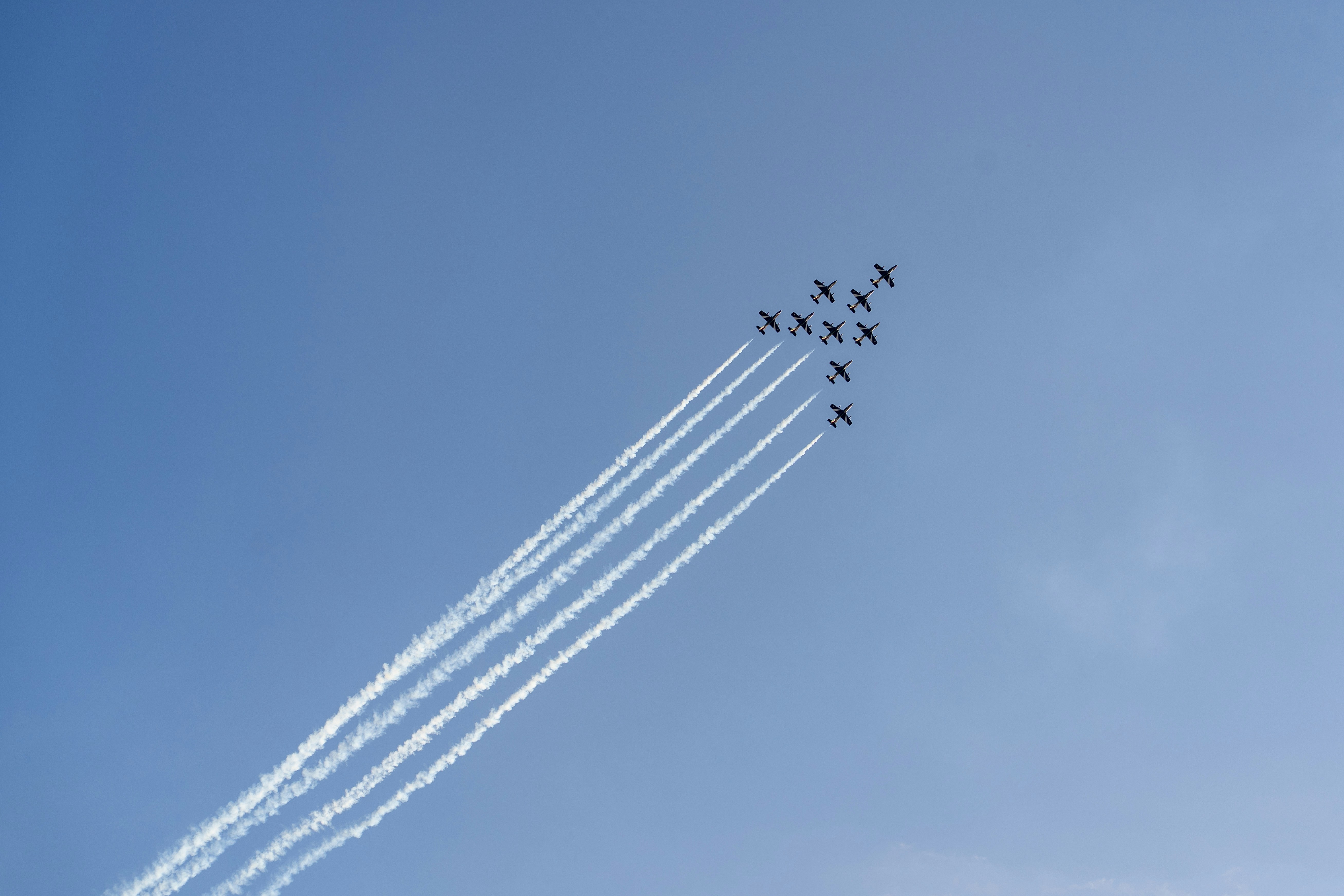 A formation of nine jet planes leaving white contrails against a clear blue sky