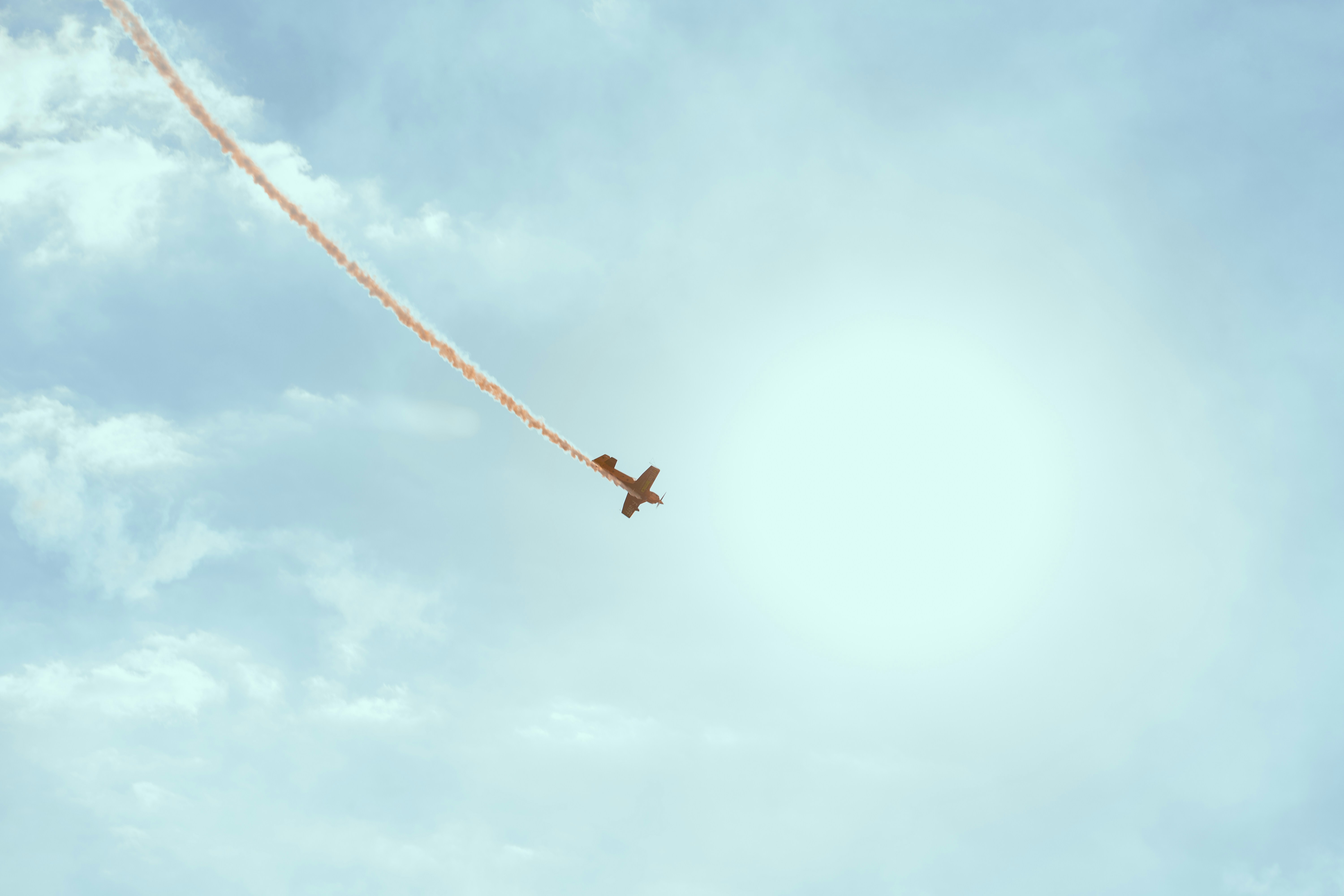 A small stunt plane flying through a blue sky with a long orange smoke trail