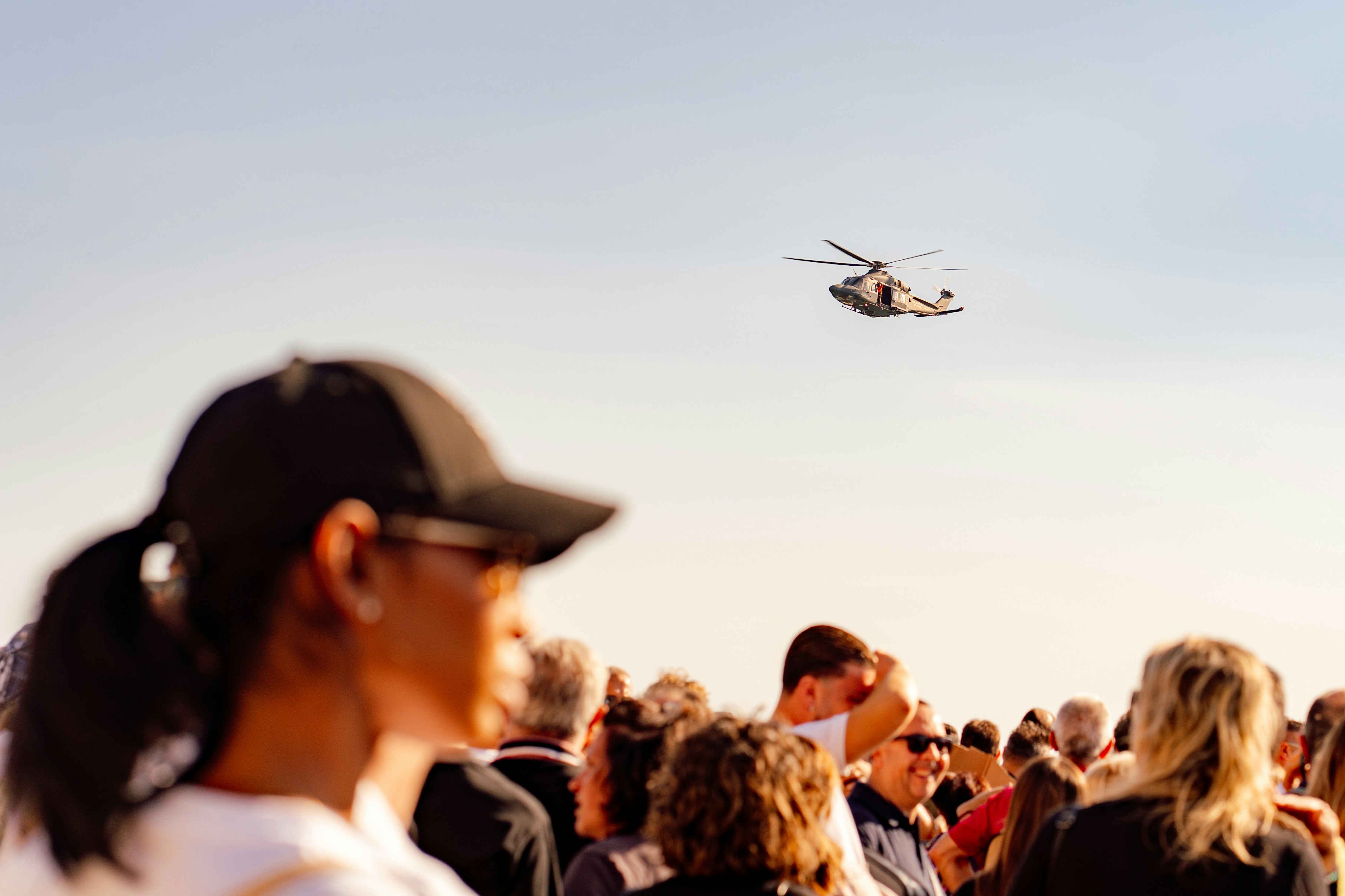 A helicopter flying over a crowd of people under a clear sky