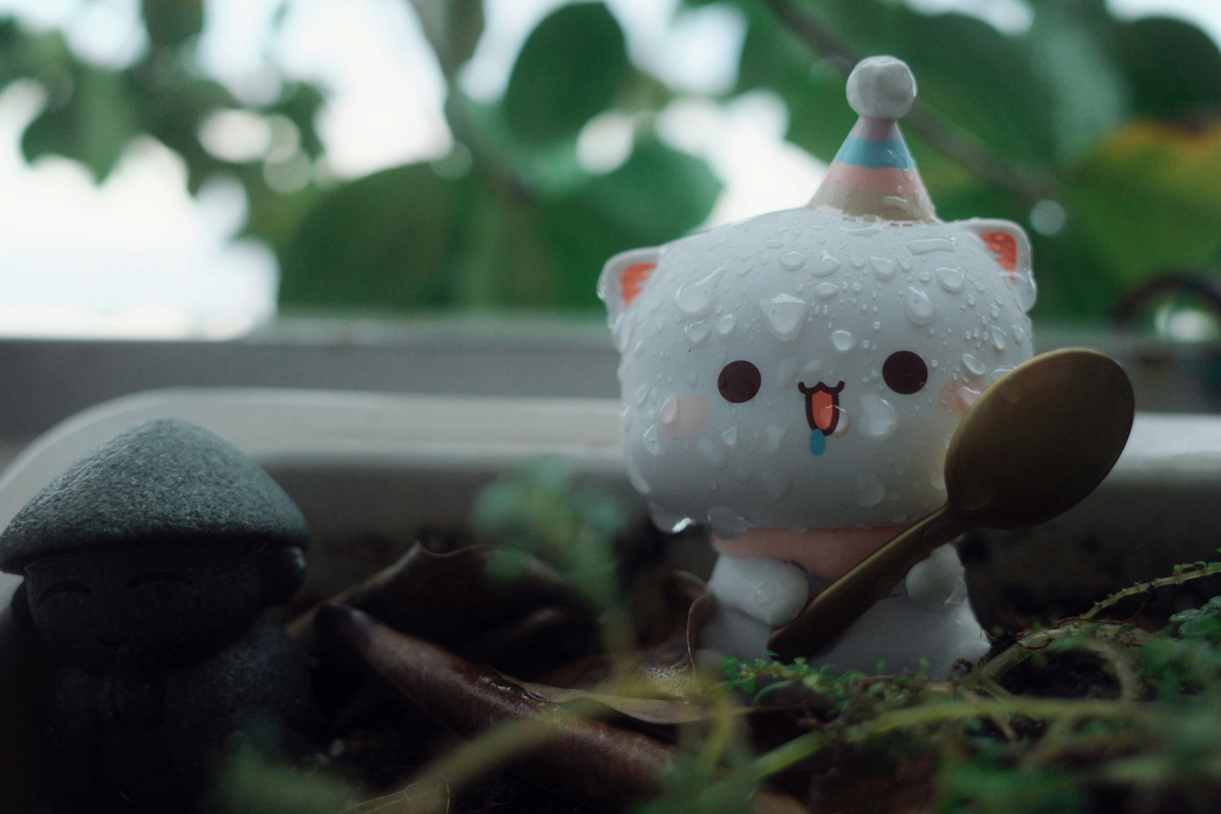 A wet white cat figurine wearing a party hat and holding a spoon
