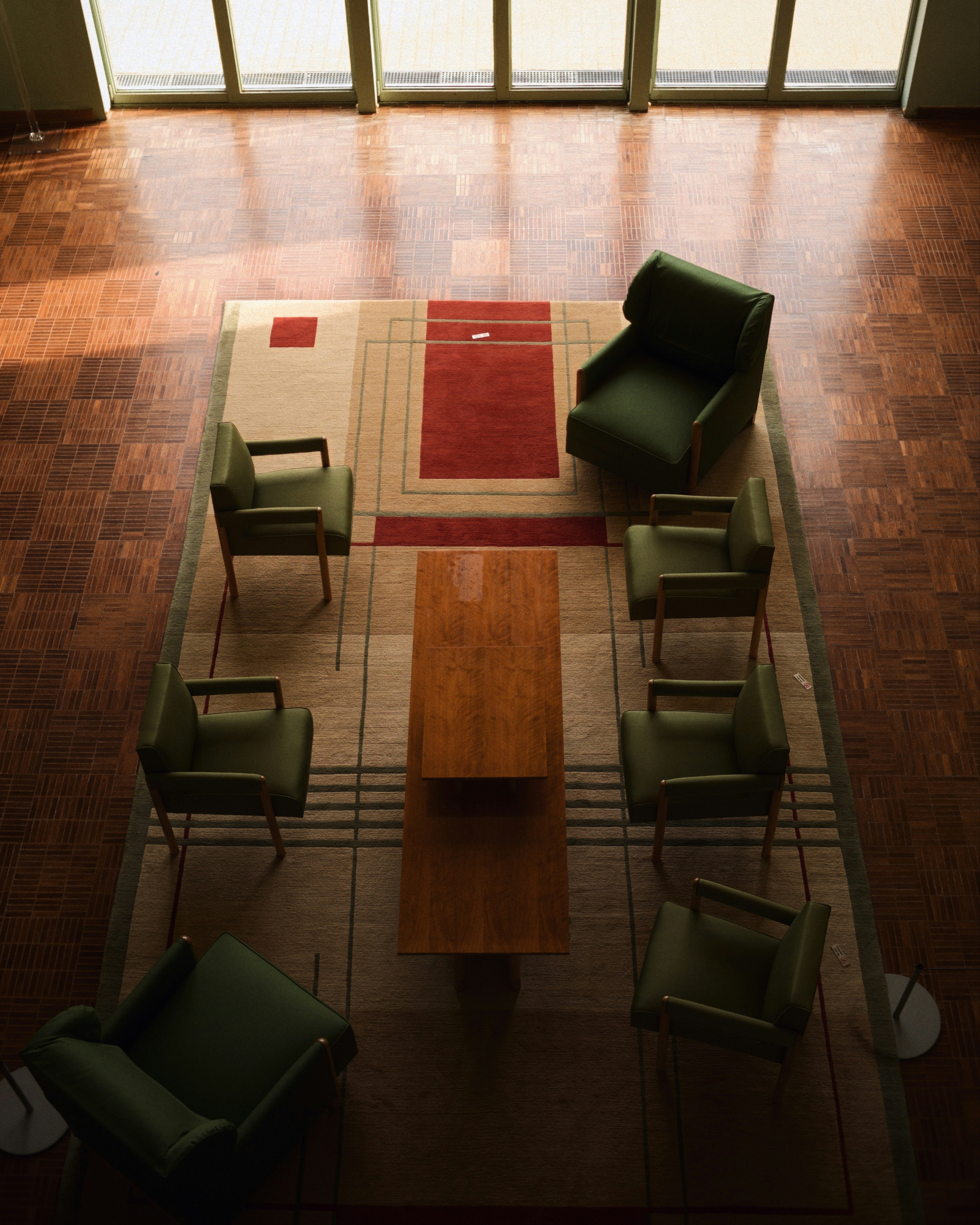 Six green armchairs arranged around a long wooden table on a geometric rug