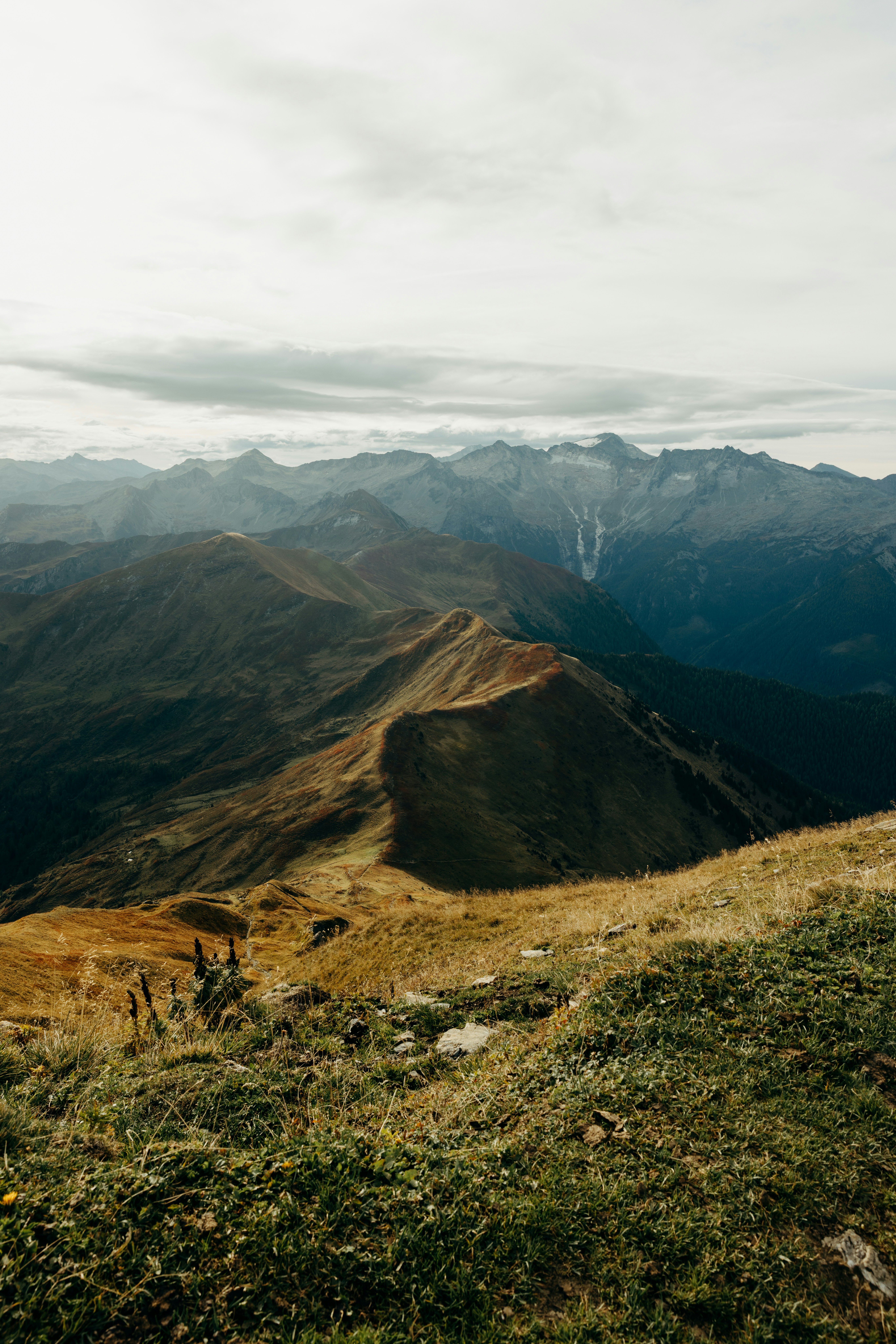 A grassy mountain ridge leading toward distant peaks under a cloudy sky