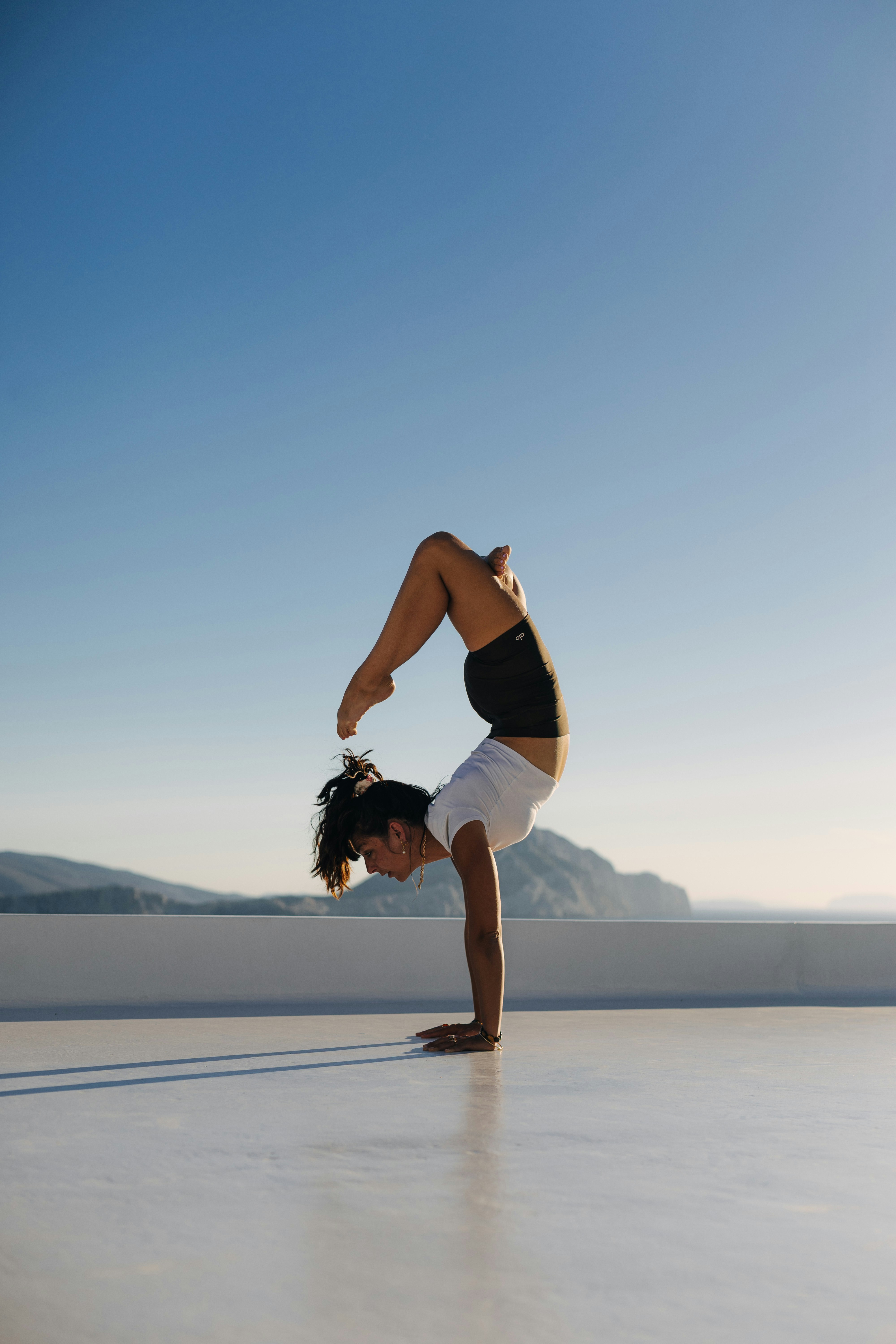 A woman in a white top and black shorts performing a handstand on a terrace