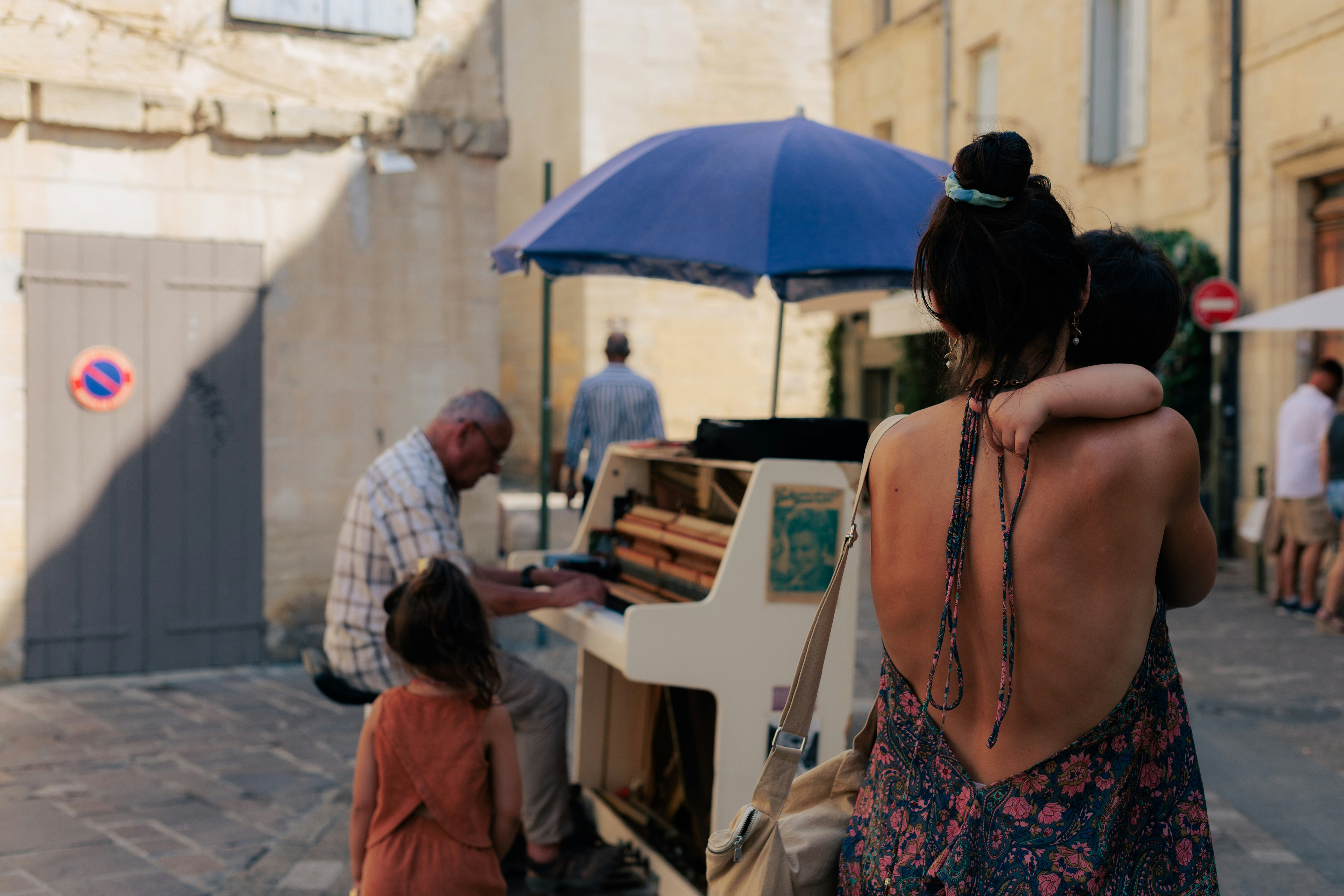 A woman holding a child watching a man play a street piano