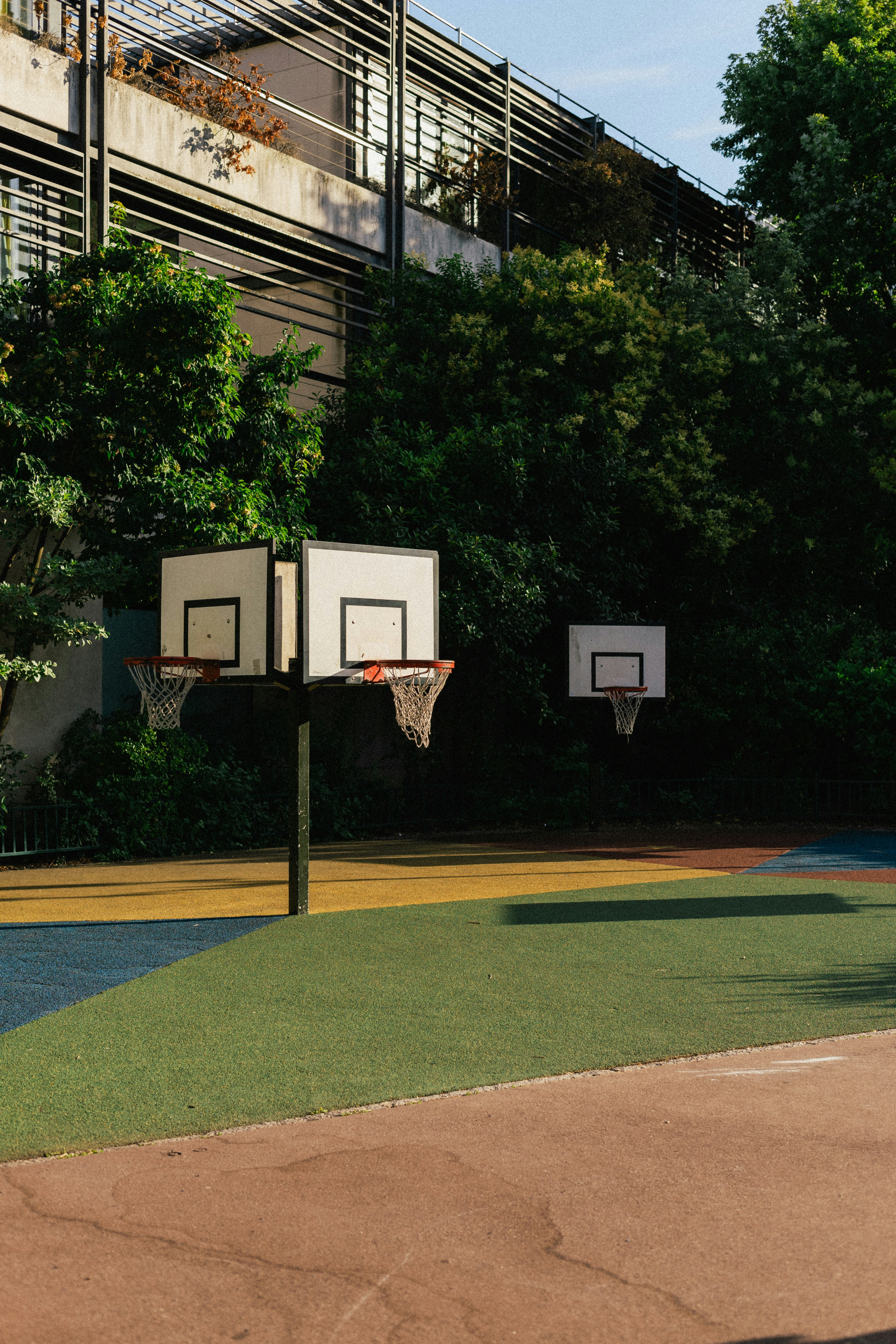 Basketball hoops on a colorful outdoor court with trees and a building behind