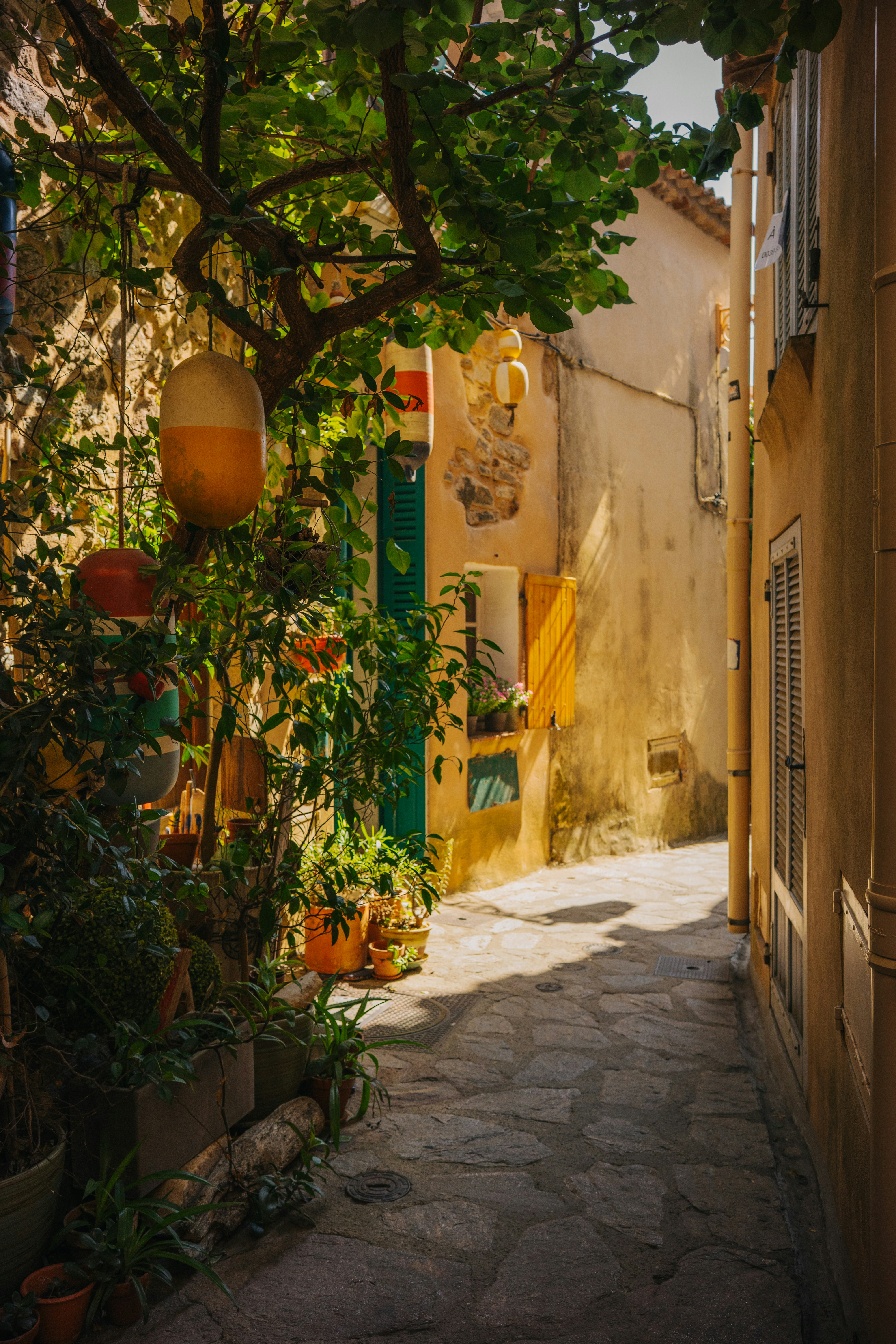 A narrow stone alleyway with yellow walls and hanging fishing buoys in a village
