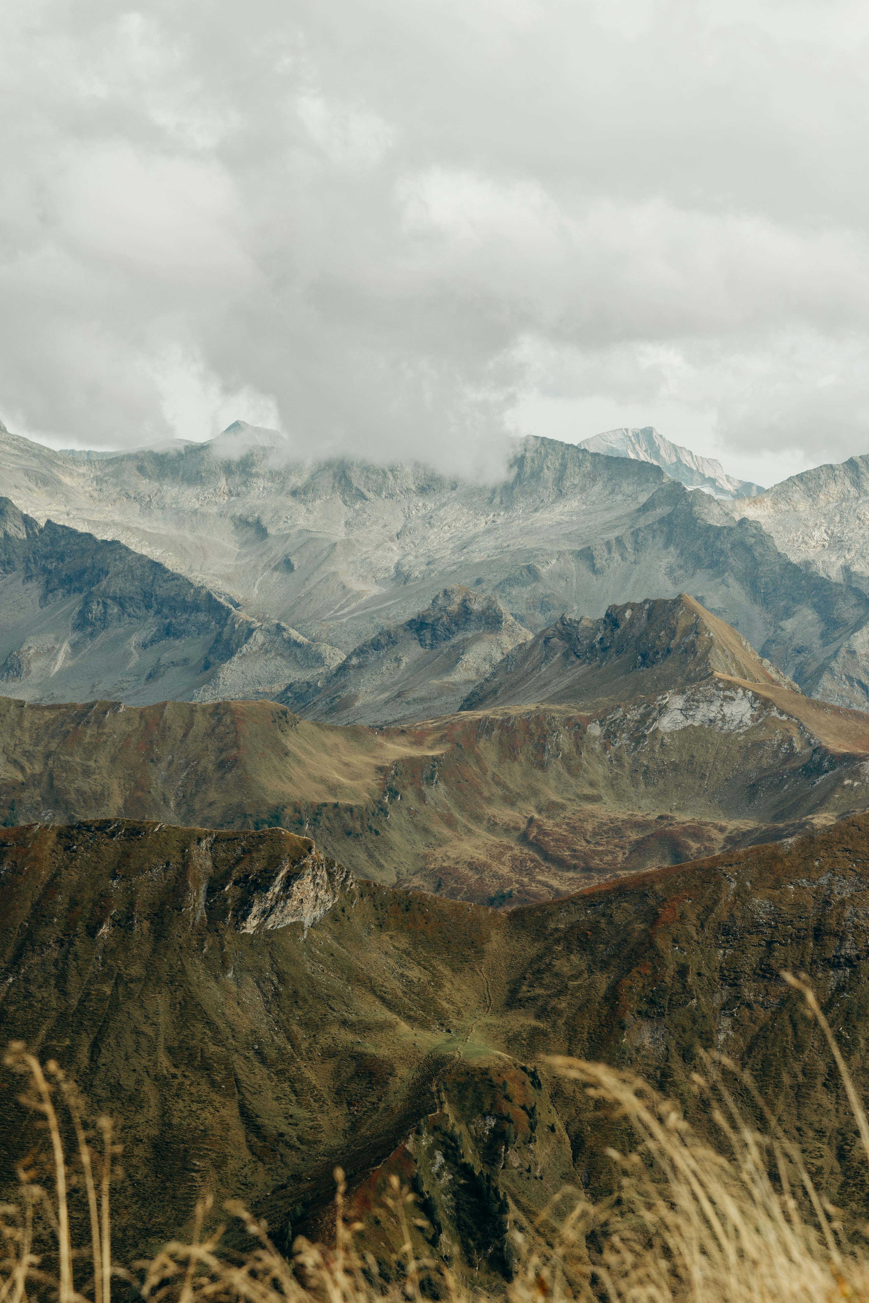Rugged mountain peaks under a cloudy sky with dry grass in the foreground