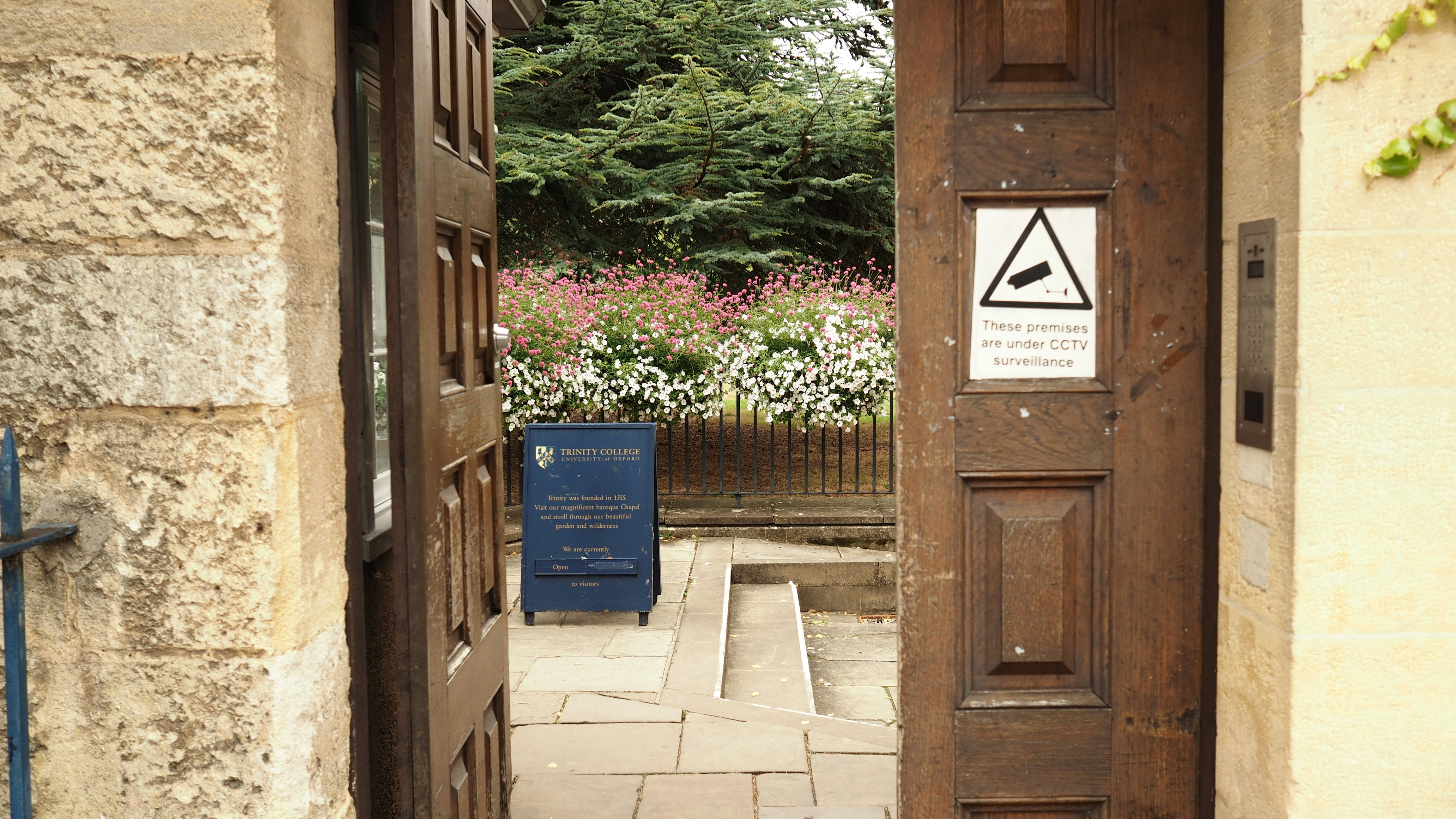 An open wooden gate at Trinity College in Oxford with a CCTV warning sign