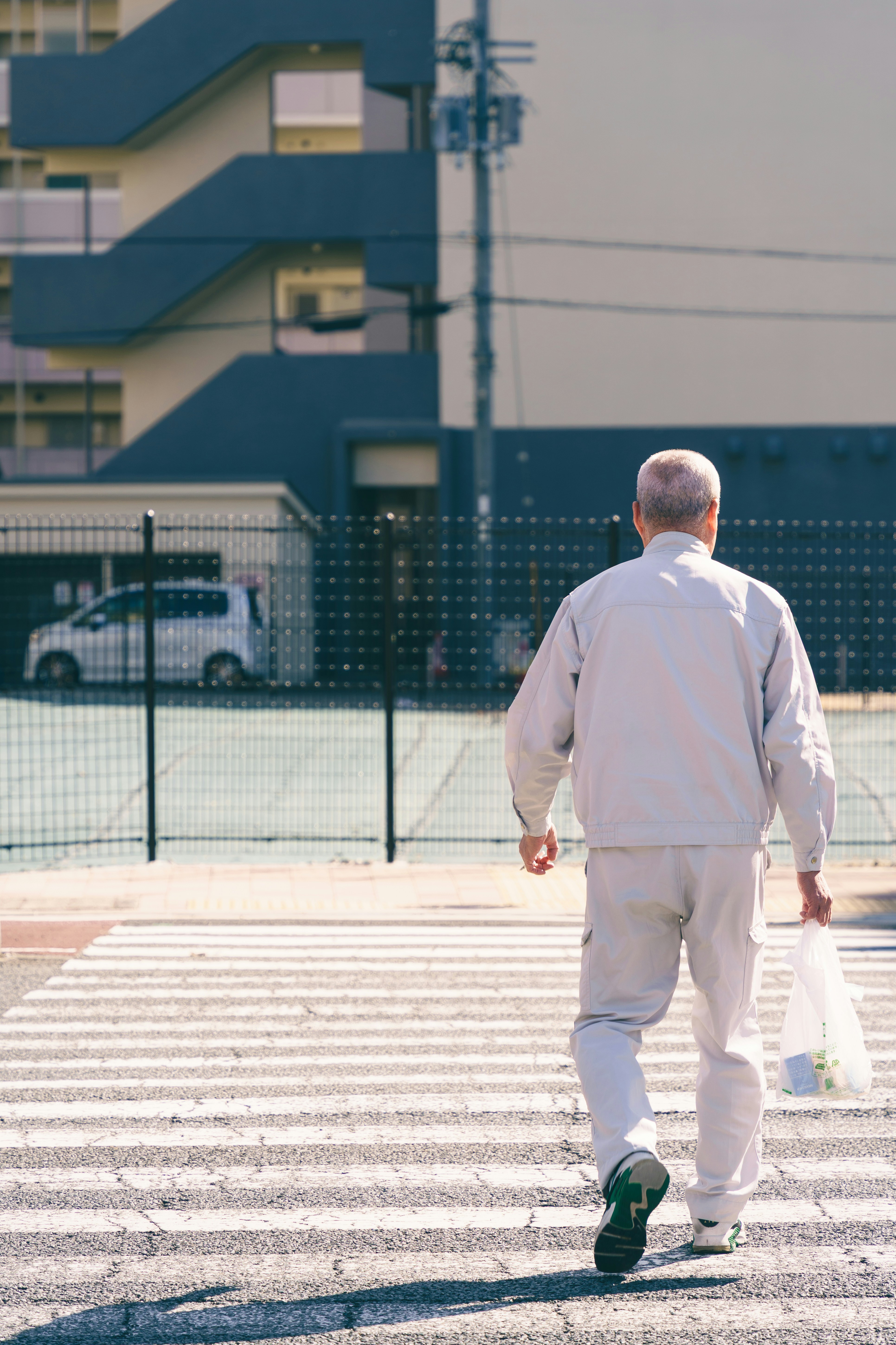 An older man in a light grey uniform walking across a pedestrian crossing