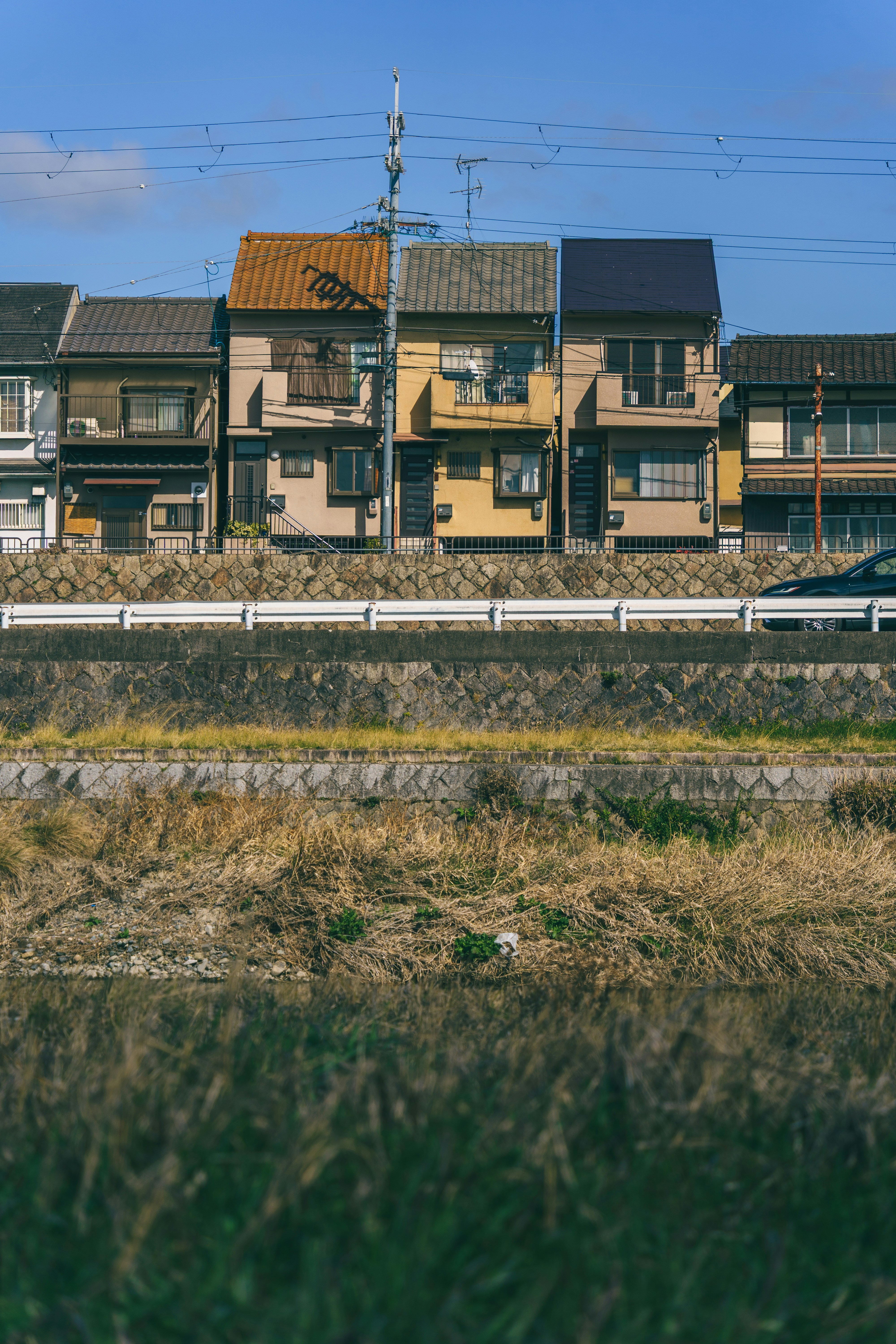 A row of houses behind a stone embankment and a grassy riverbank