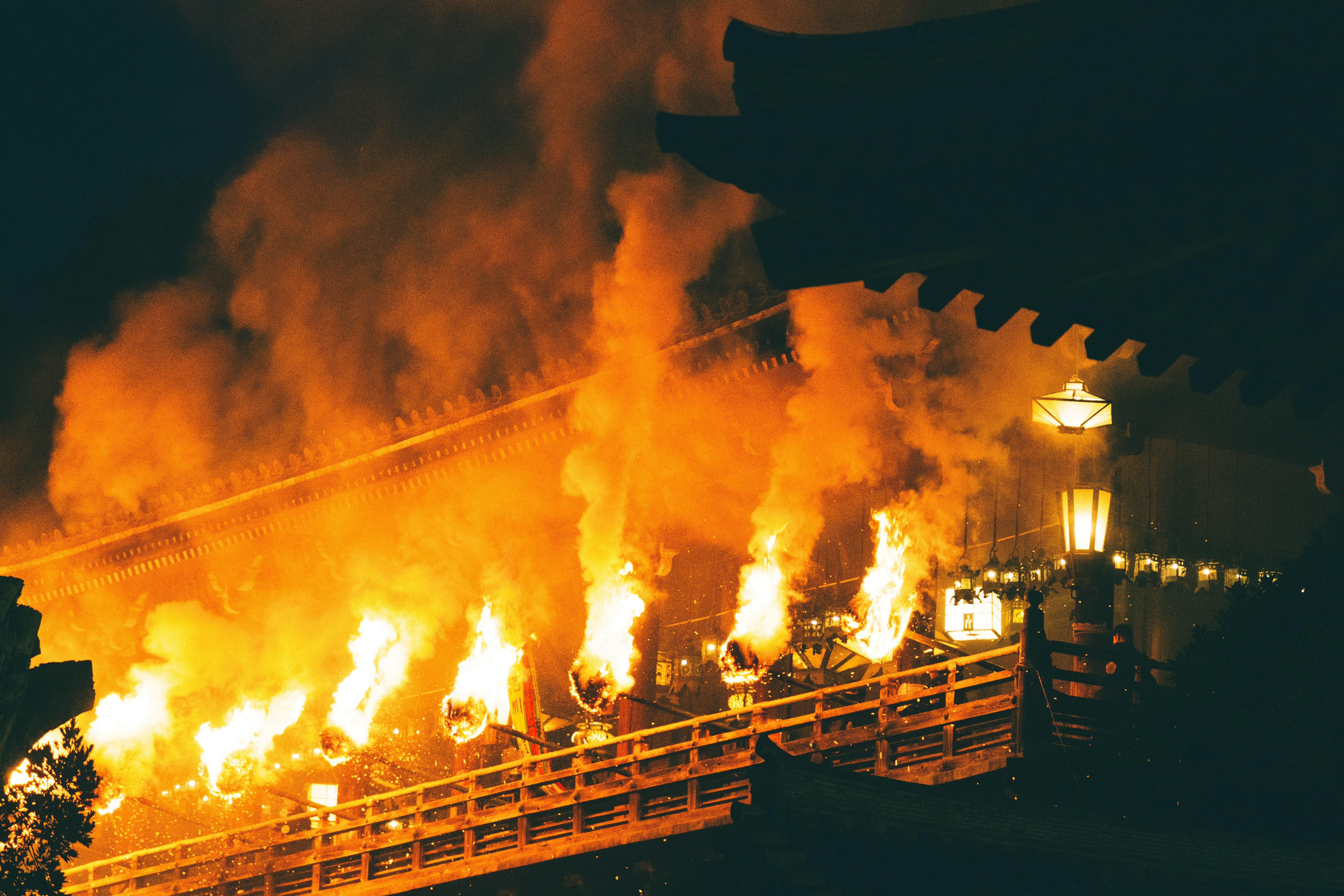 Bright flames rising from torches along a wooden temple walkway at night