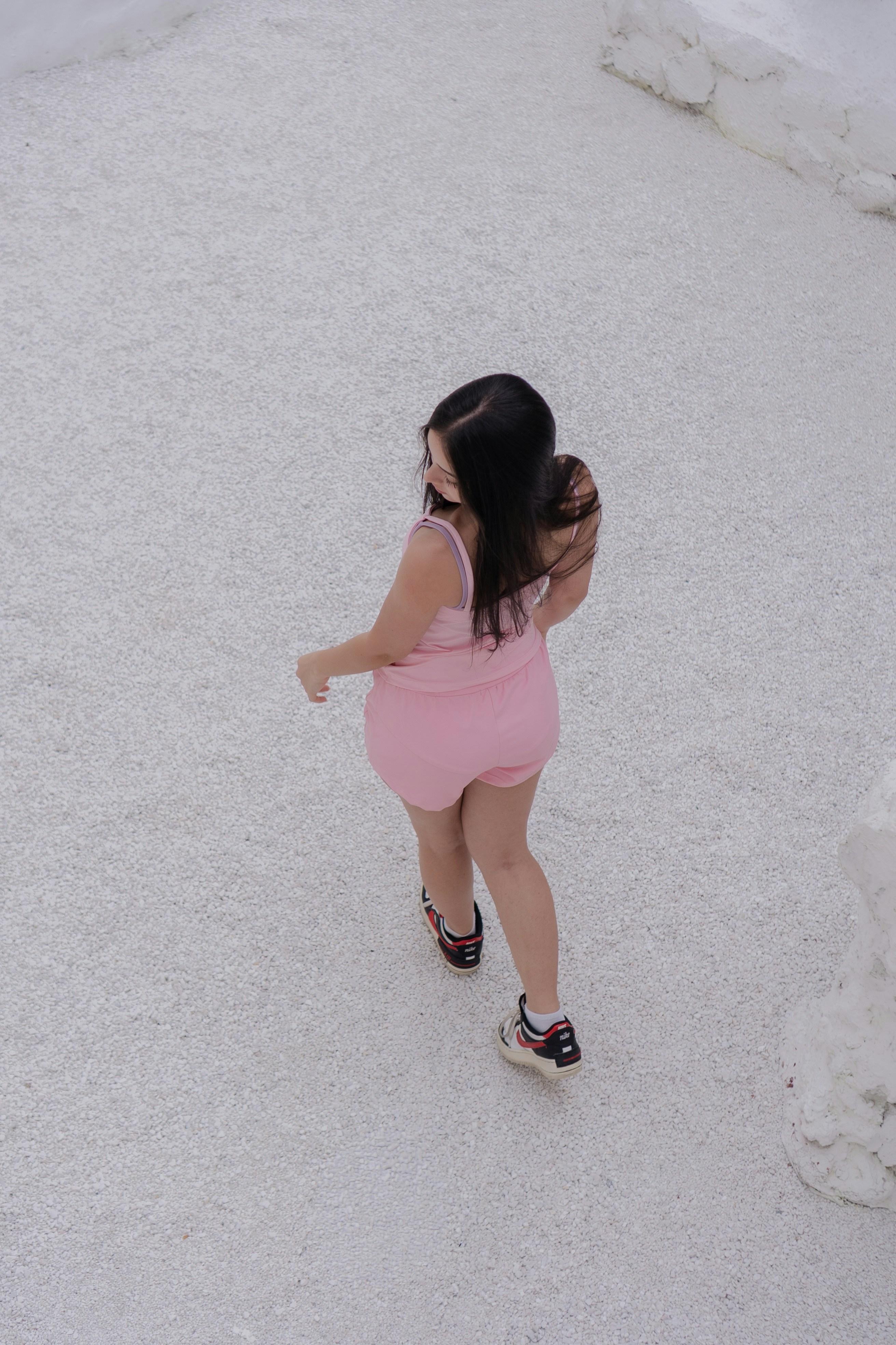 A woman in a pink tank top and shorts walking on white gravel