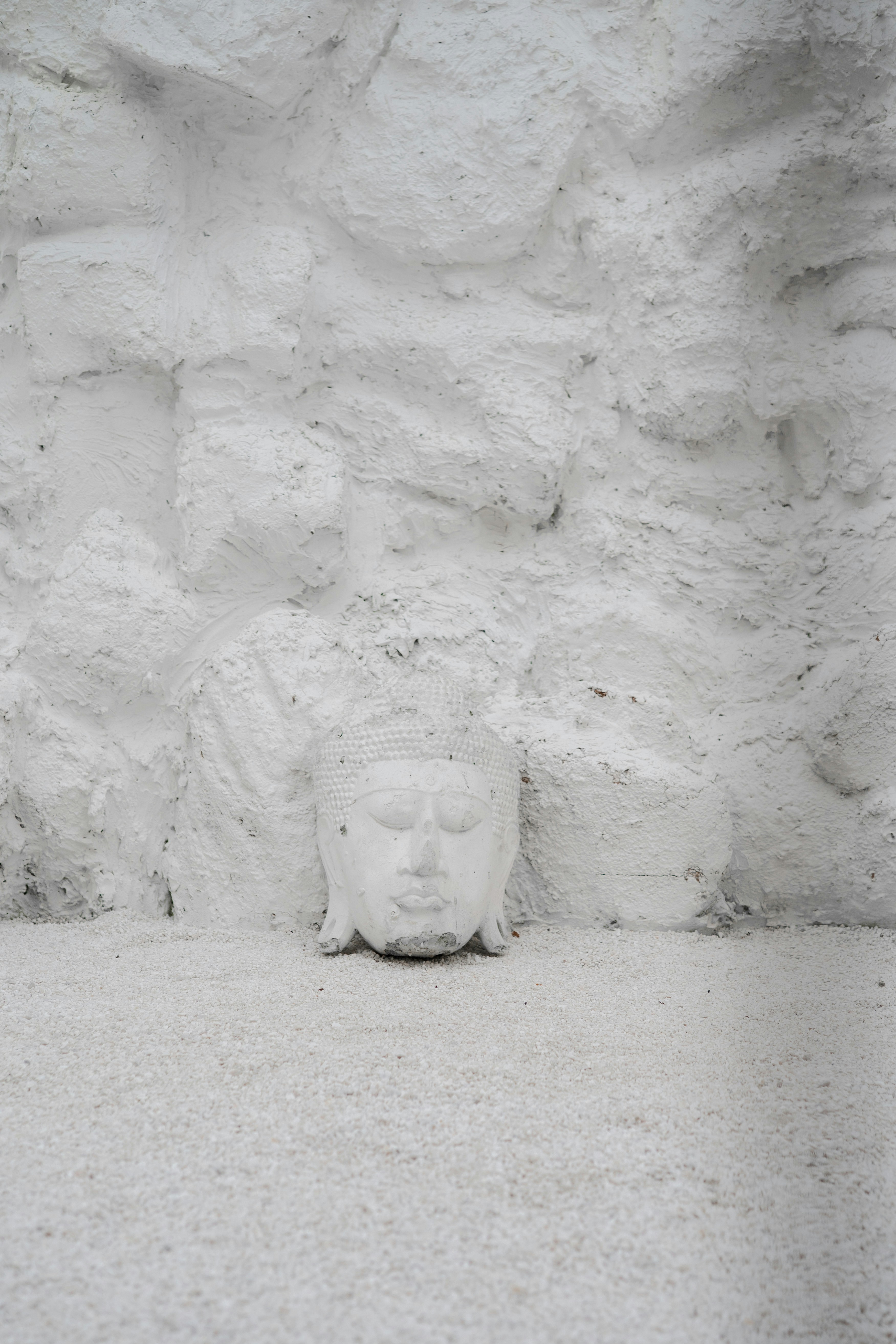 A white Buddha head sculpture against a textured white stone wall