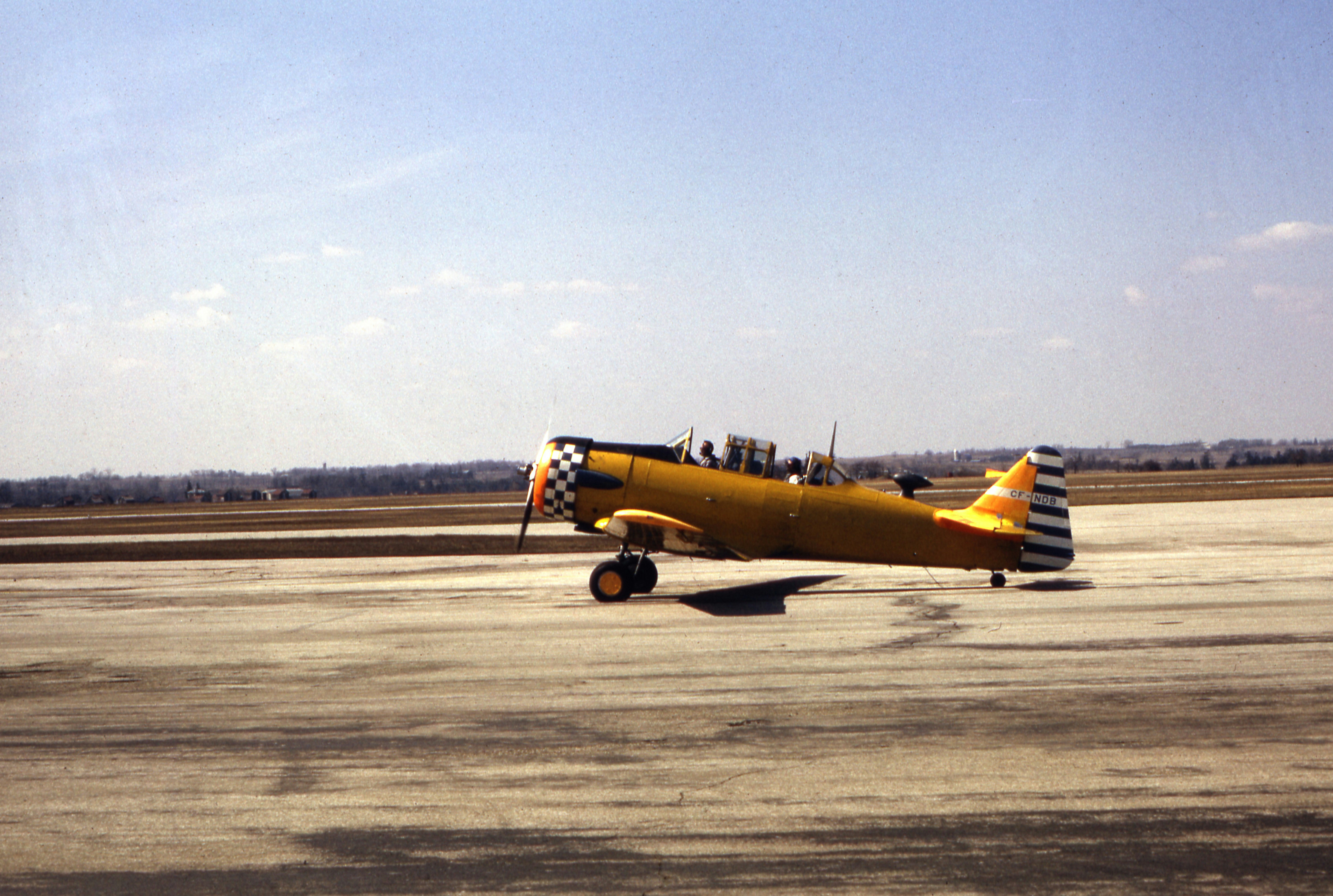 A yellow vintage propeller airplane taxiing on a concrete airfield under a clear sky