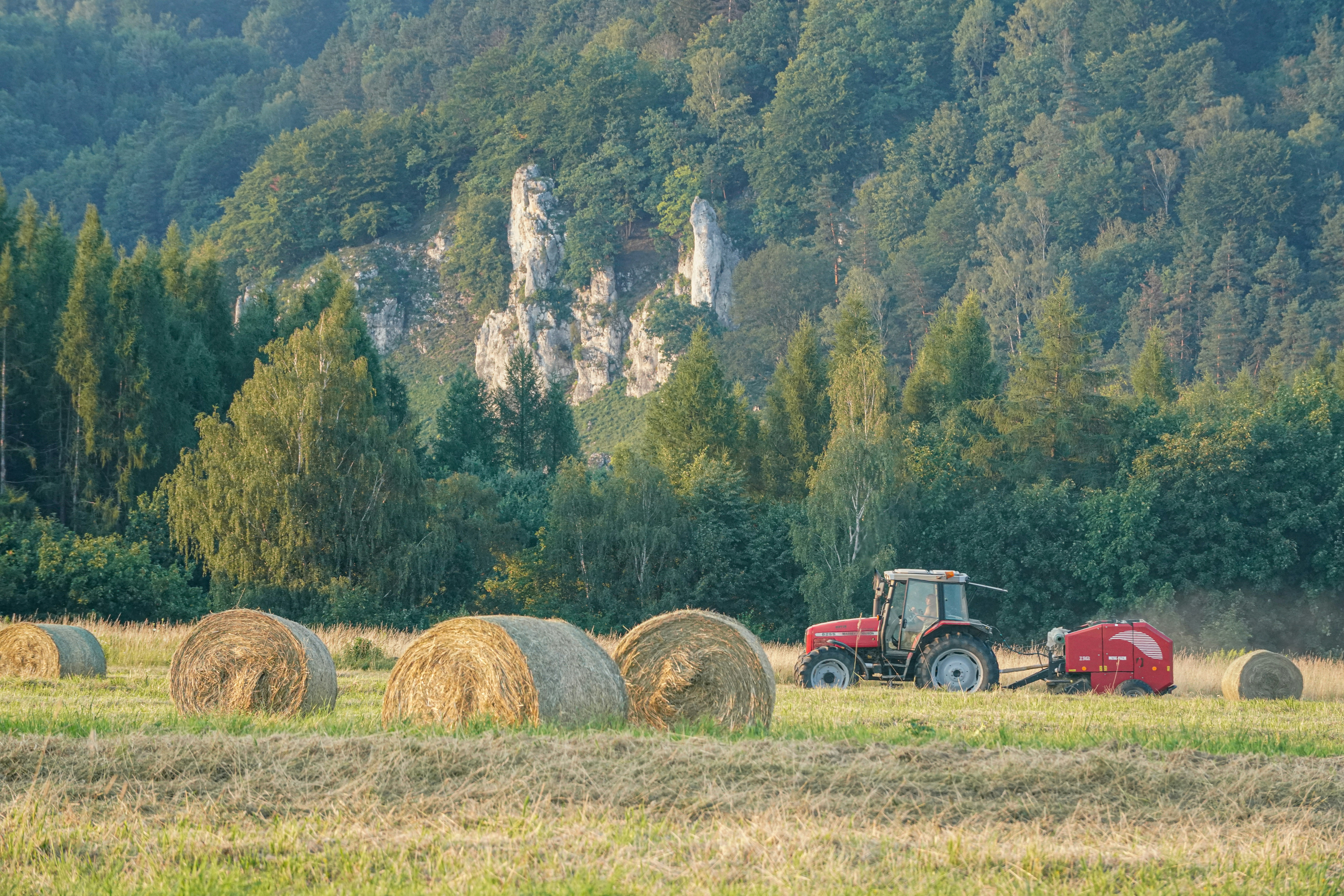 A red tractor pulling a baler through a field with hay bales