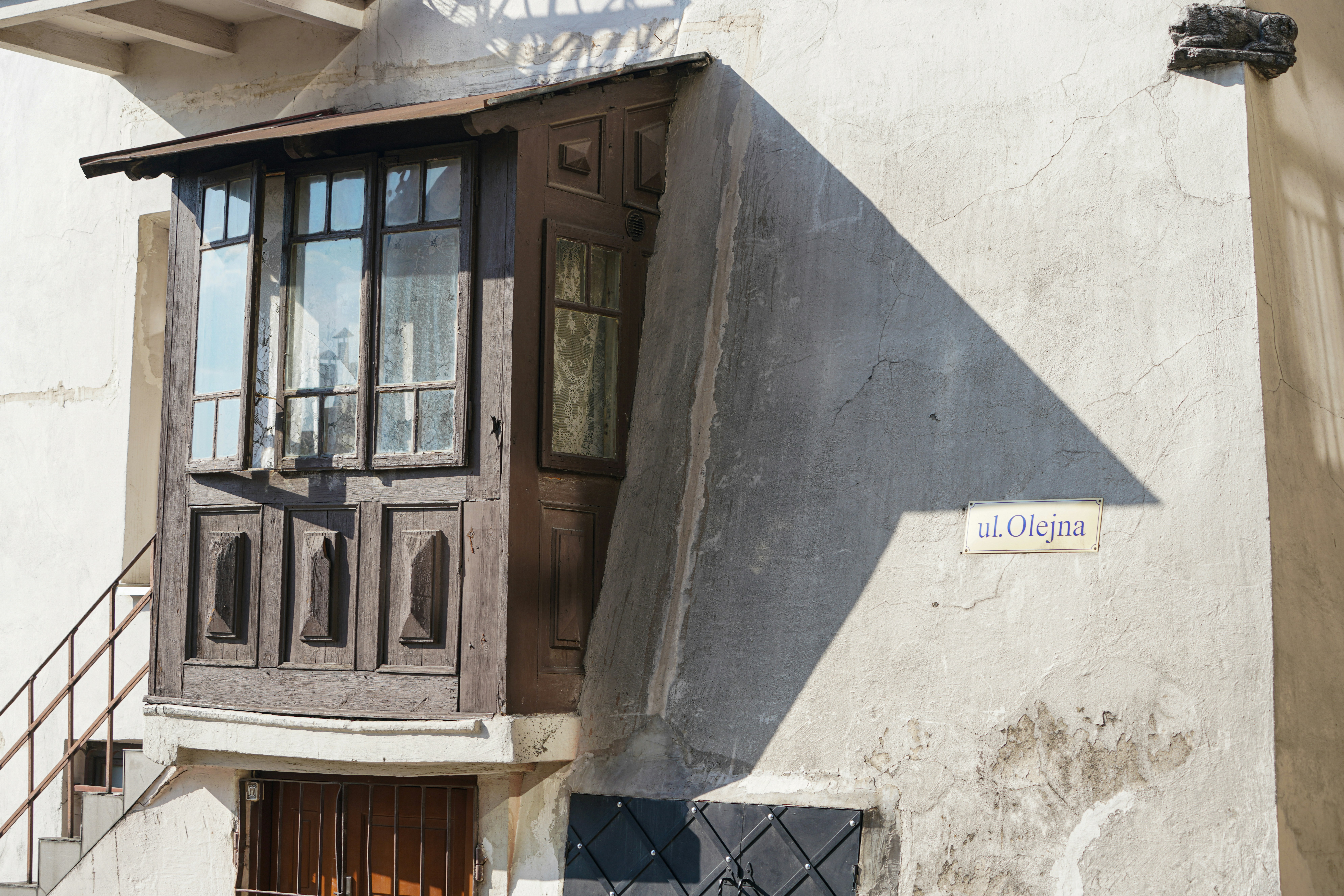 A wooden bay window on a white building with a street sign reading ul. Olejna