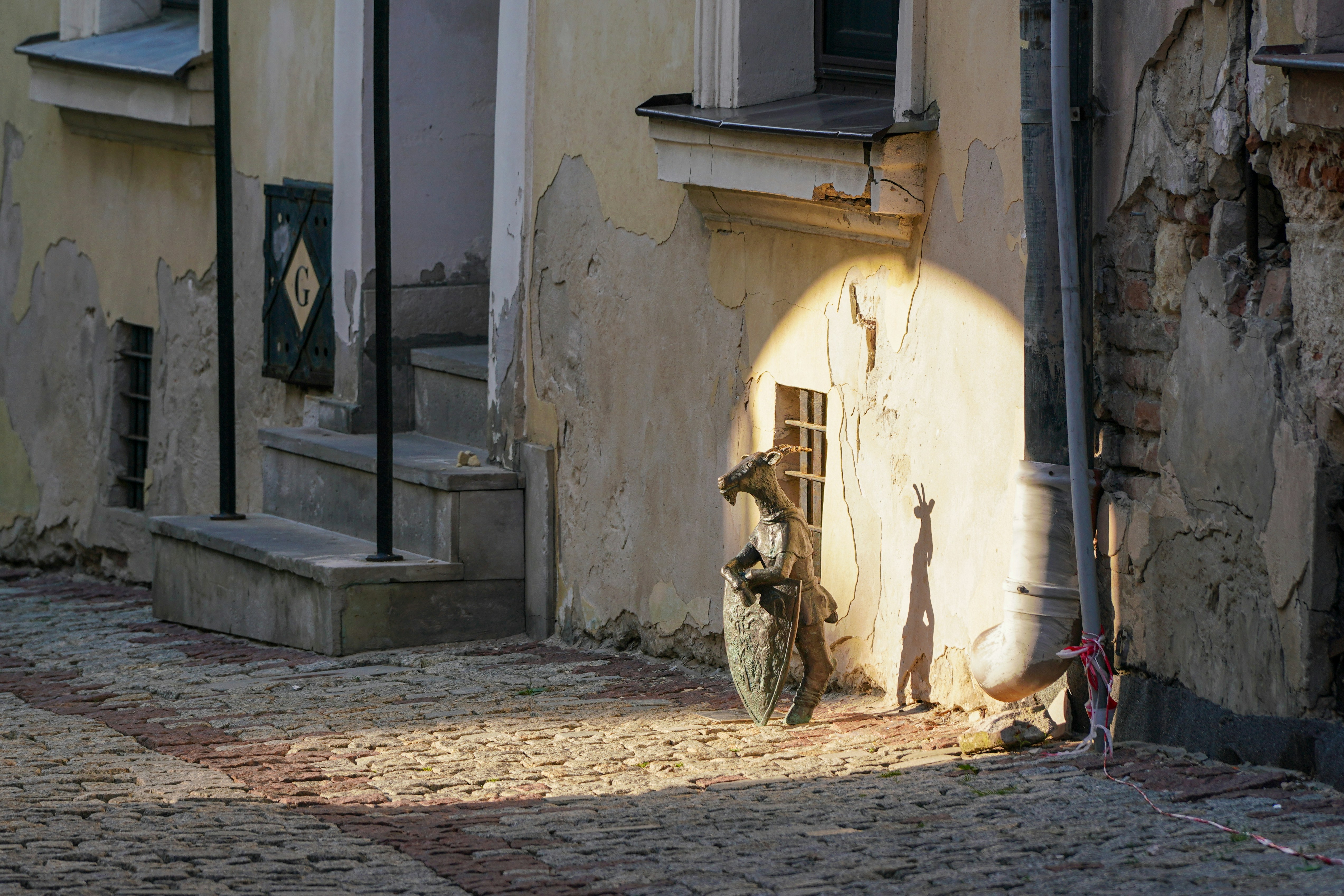 A bronze goat statue holding a shield on a cobblestone street in Poznan