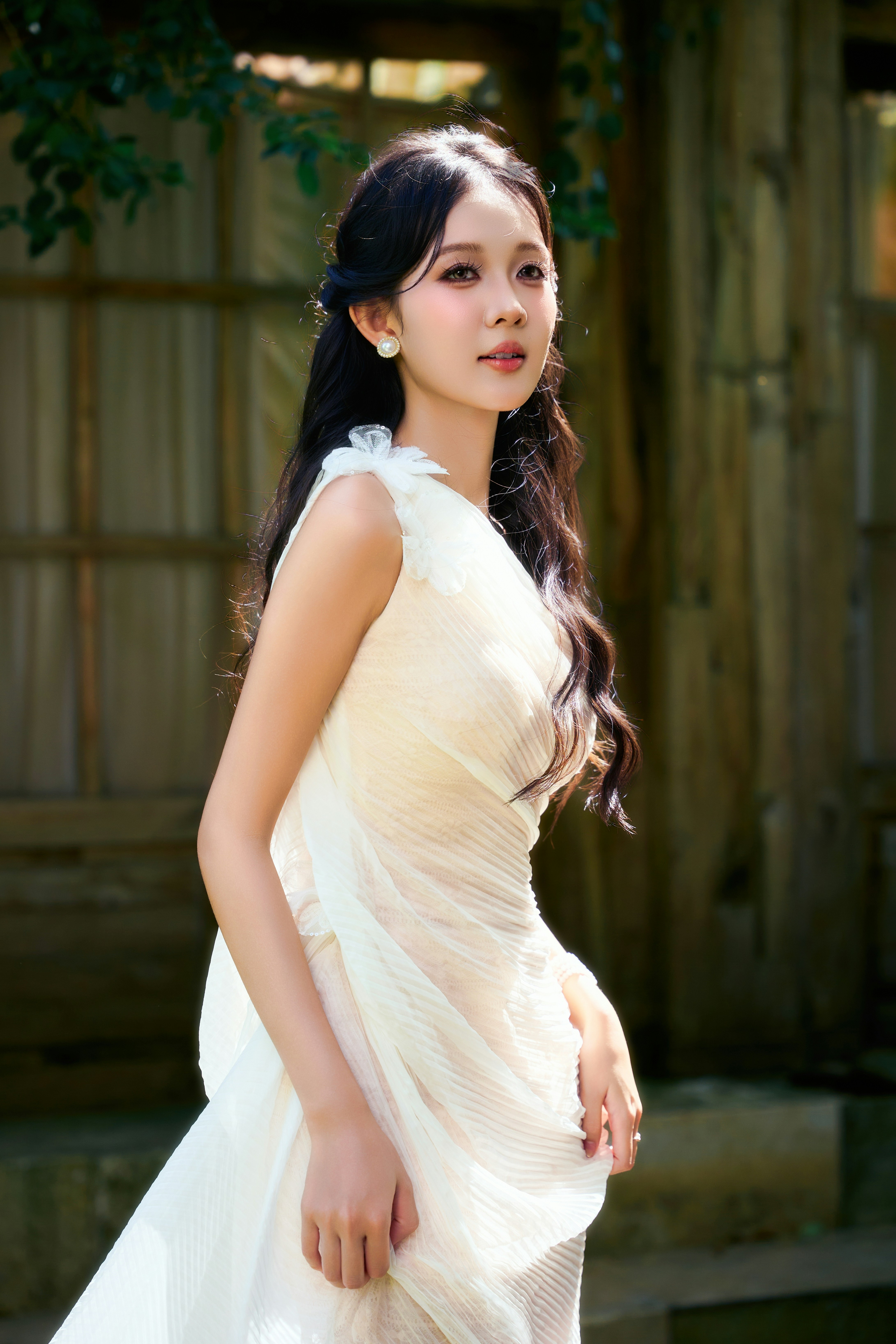 A woman with long dark hair in a white pleated dress outdoors