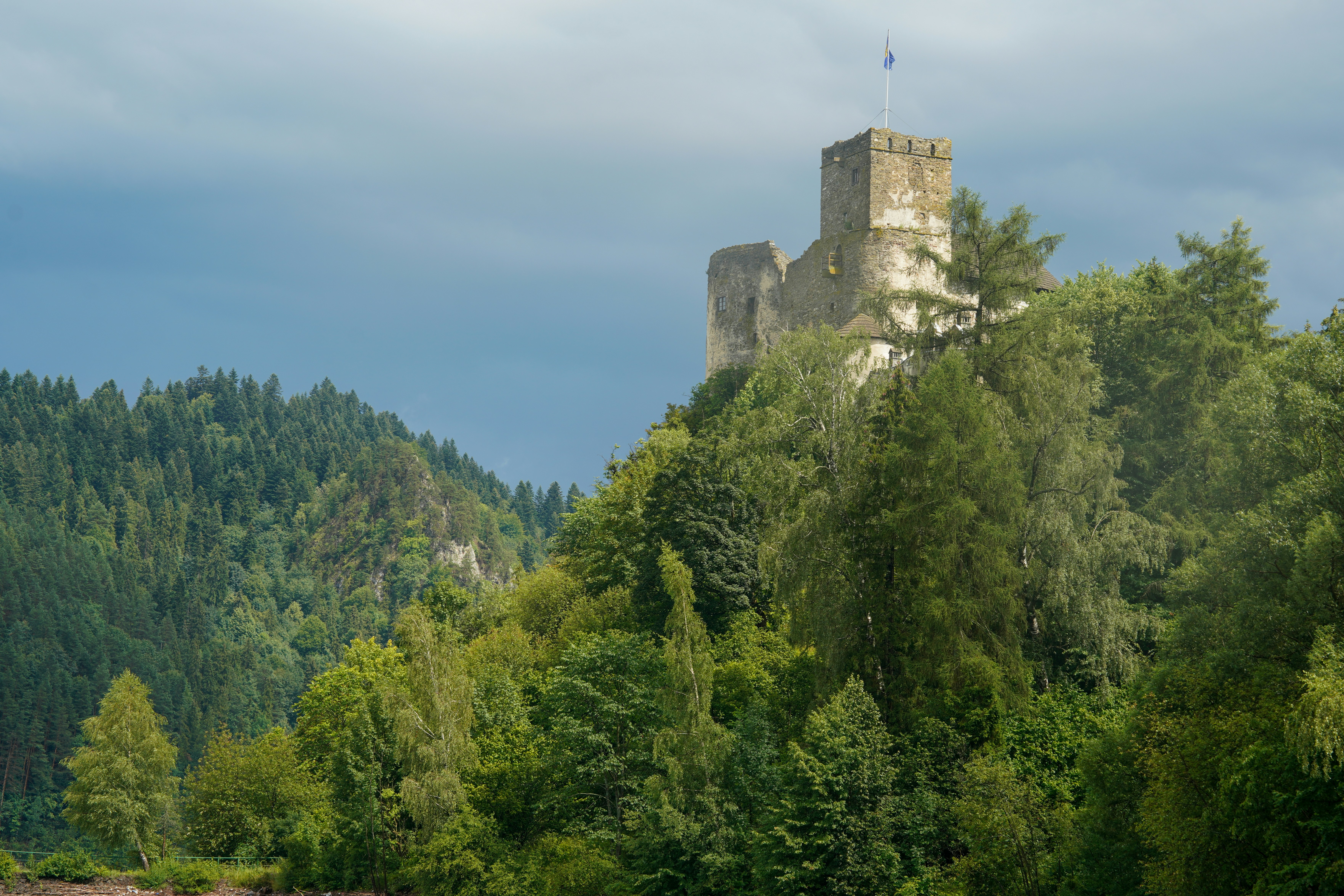 A stone castle on a forested hill under a dark cloudy sky
