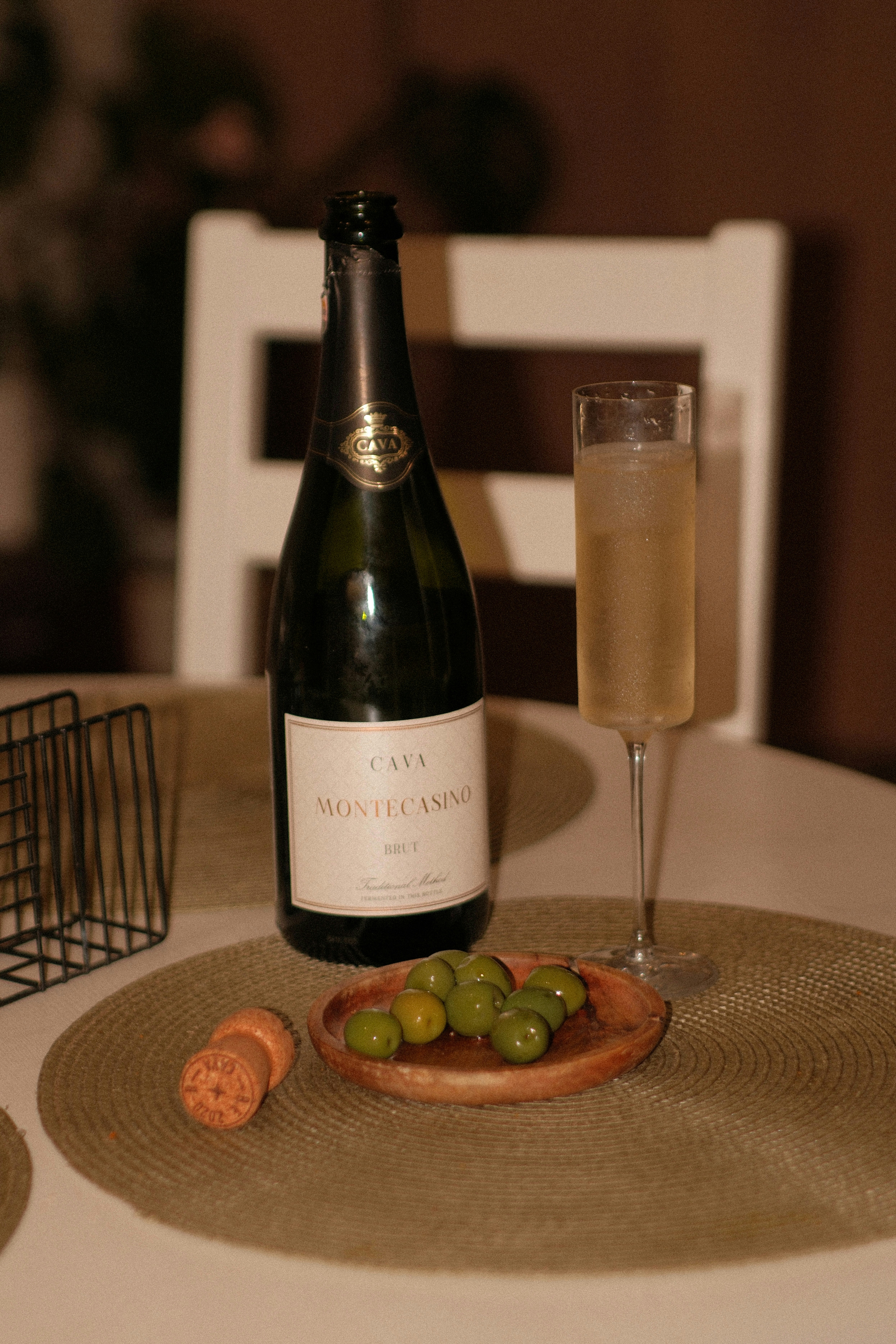 A bottle of Cava, a flute of sparkling wine, and green olives on a table