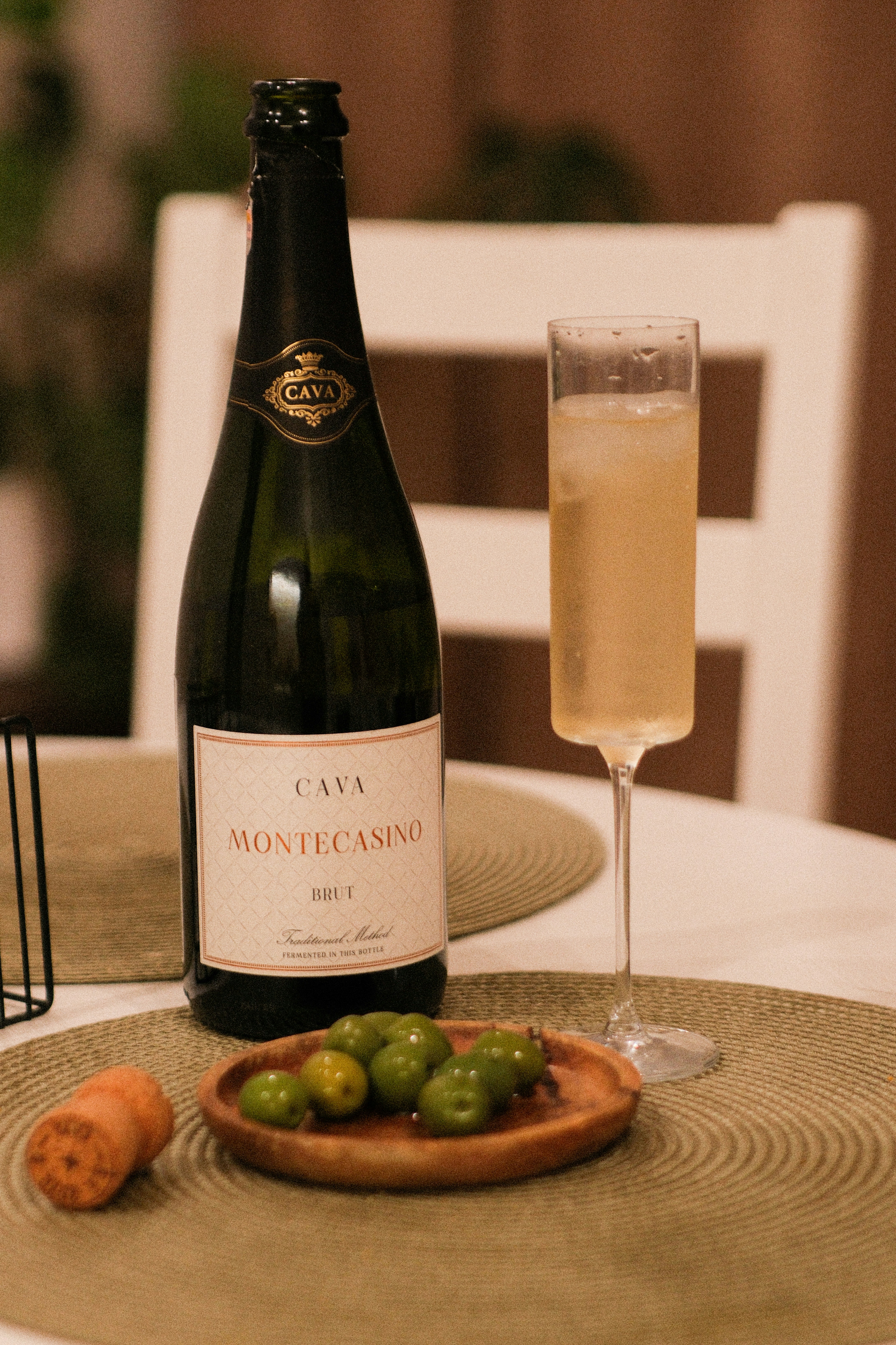 A bottle of Cava and a flute of sparkling wine with green olives