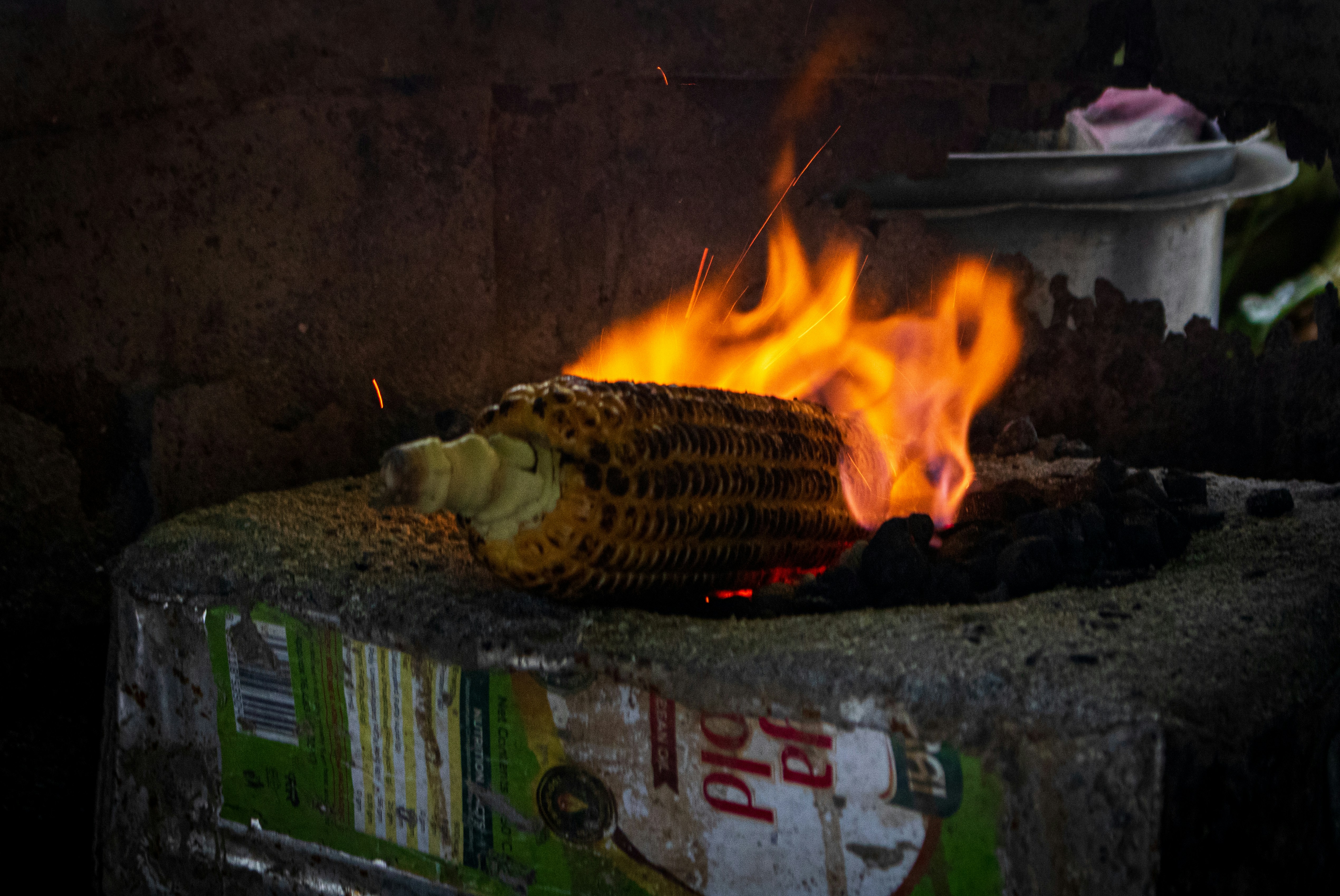 A corn cob roasting over an open flame on a stone block