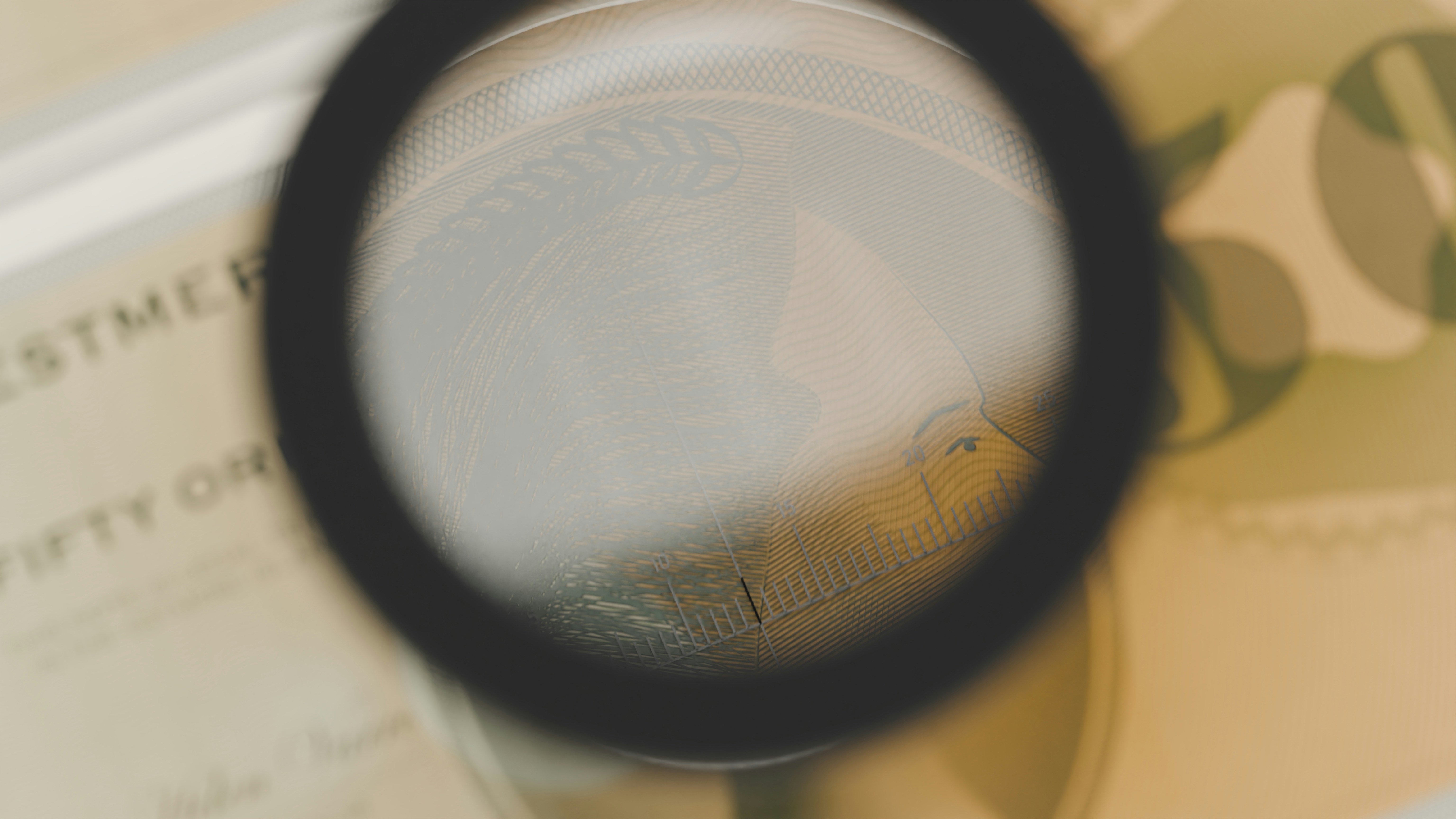 A magnifying glass over a banknote with intricate line patterns and text
