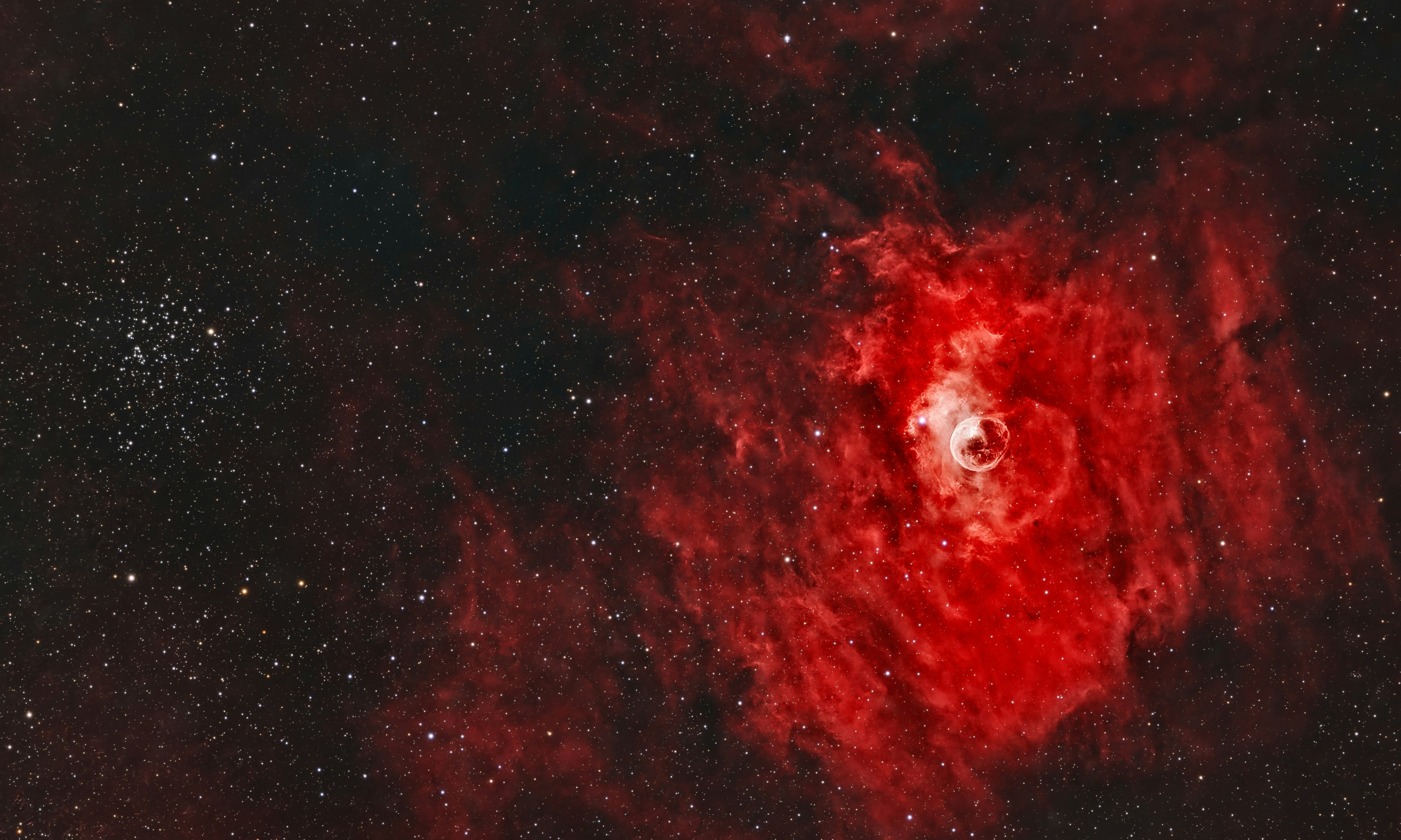 La Nebulosa Burbuja brillando en un rojo vibrante entre estrellas dispersas en el espacio profundo