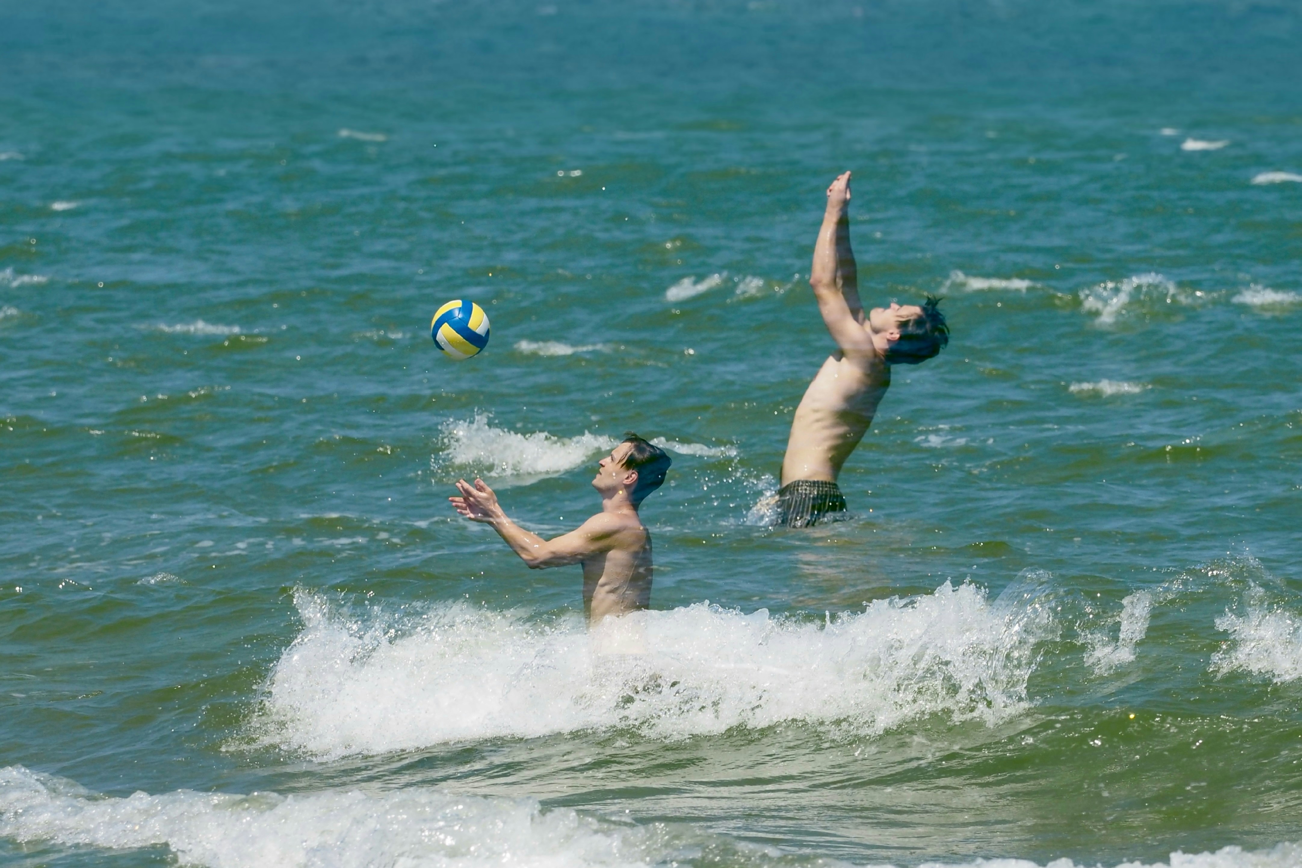Two men playing volleyball in the ocean waves