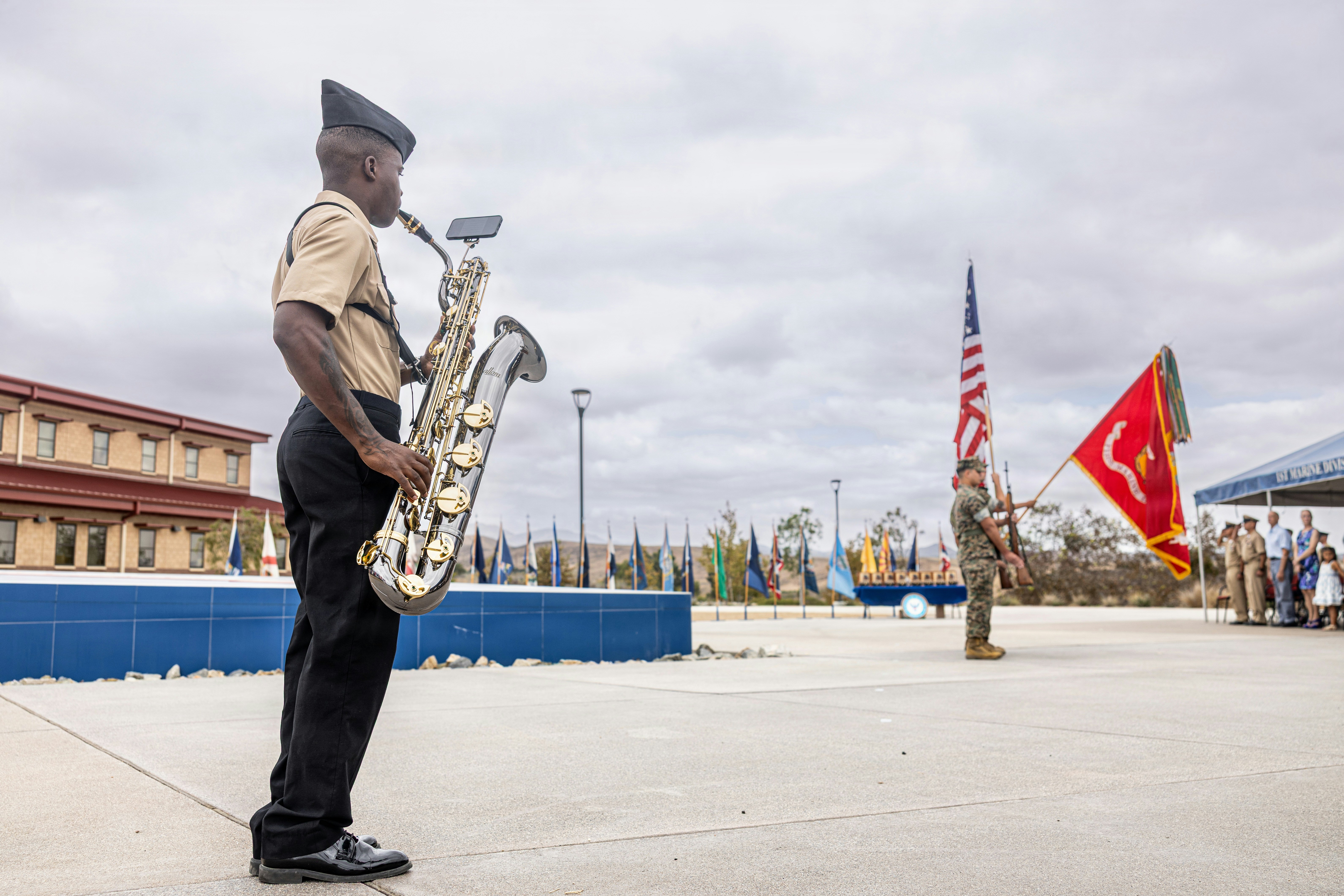 A military musician playing a saxophone at an outdoor ceremony with flags