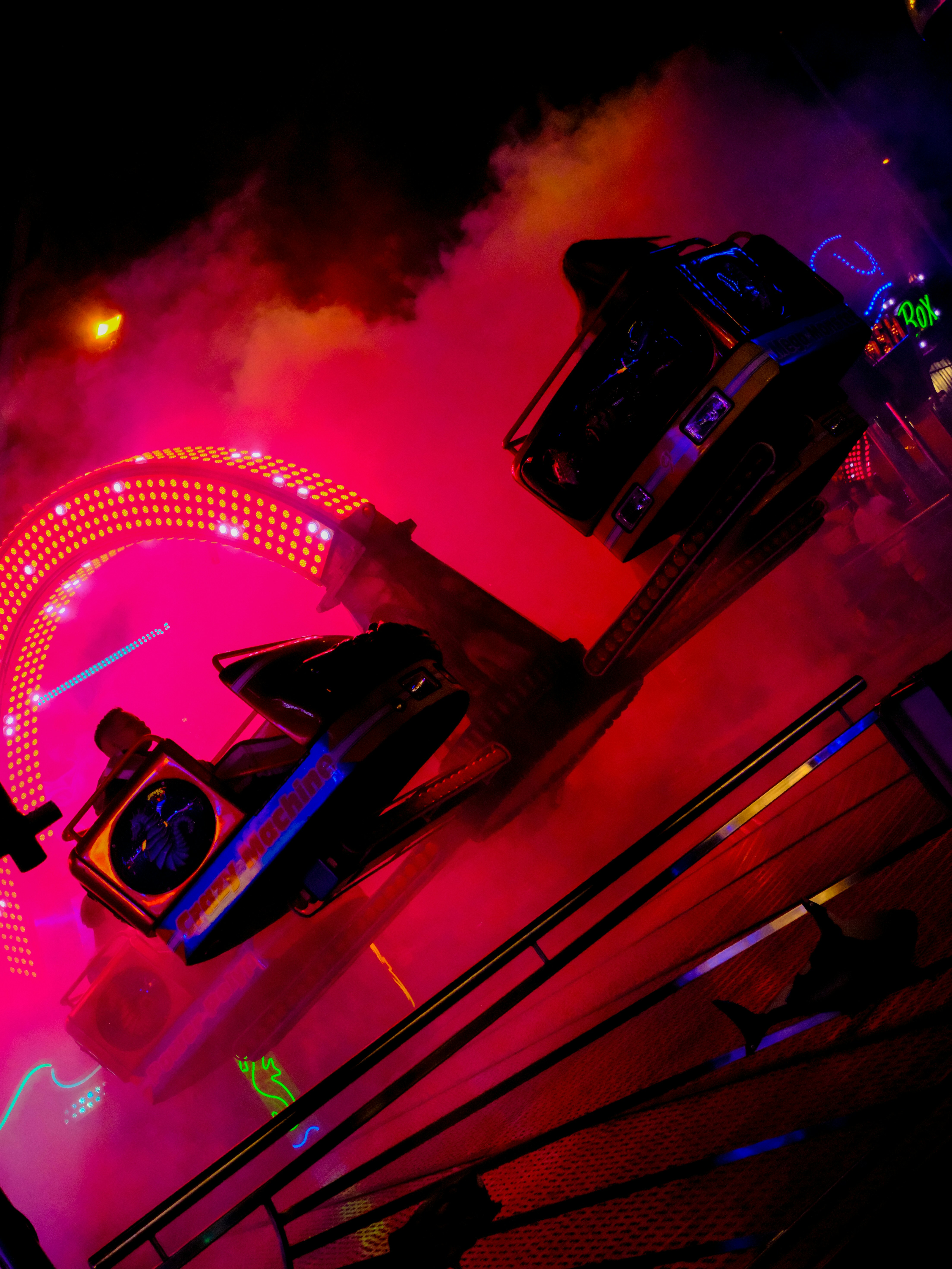 A spinning amusement park ride with bright pink lights and smoke at night