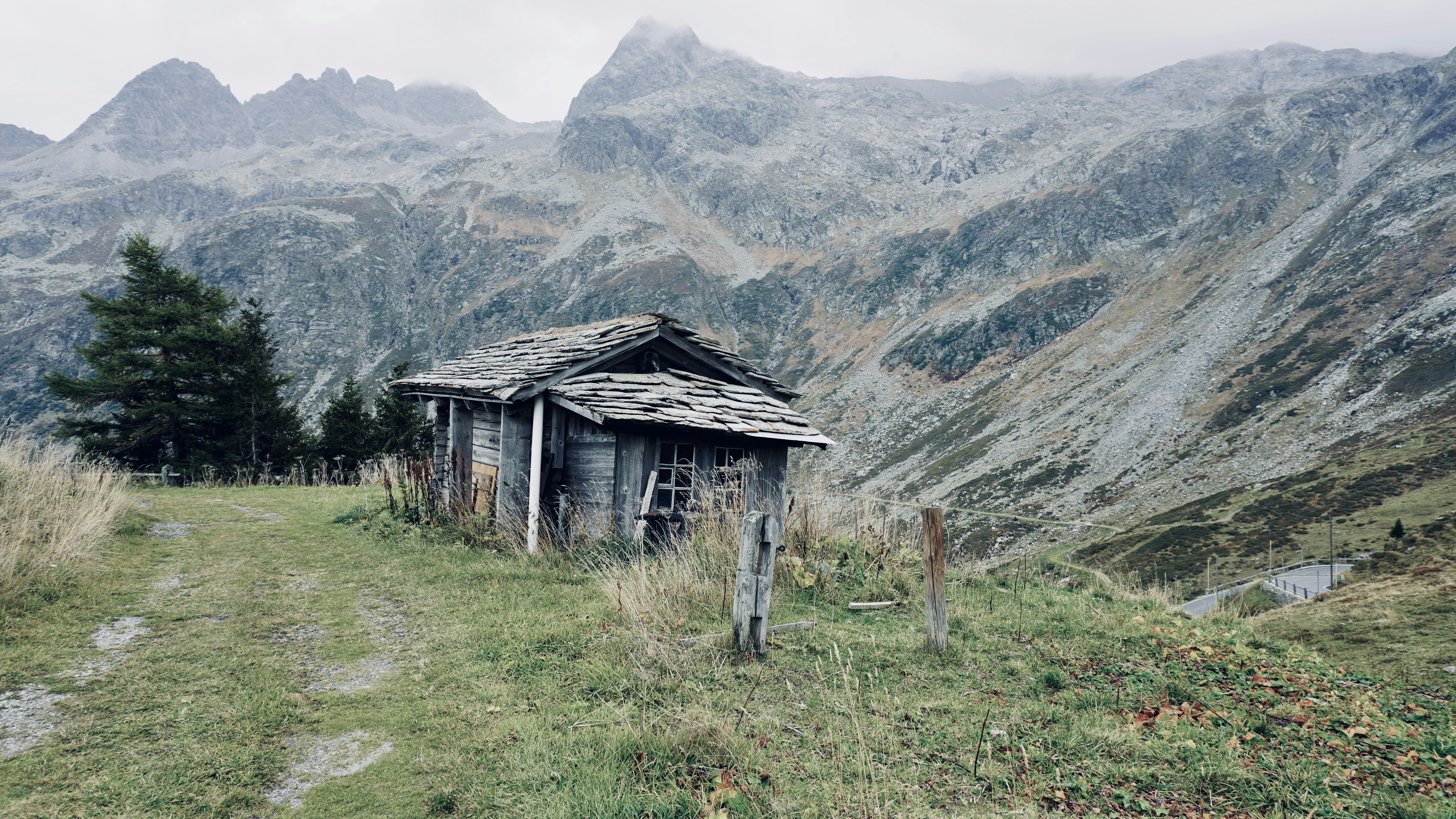 A weathered wooden cabin with a stone roof on a grassy mountain slope