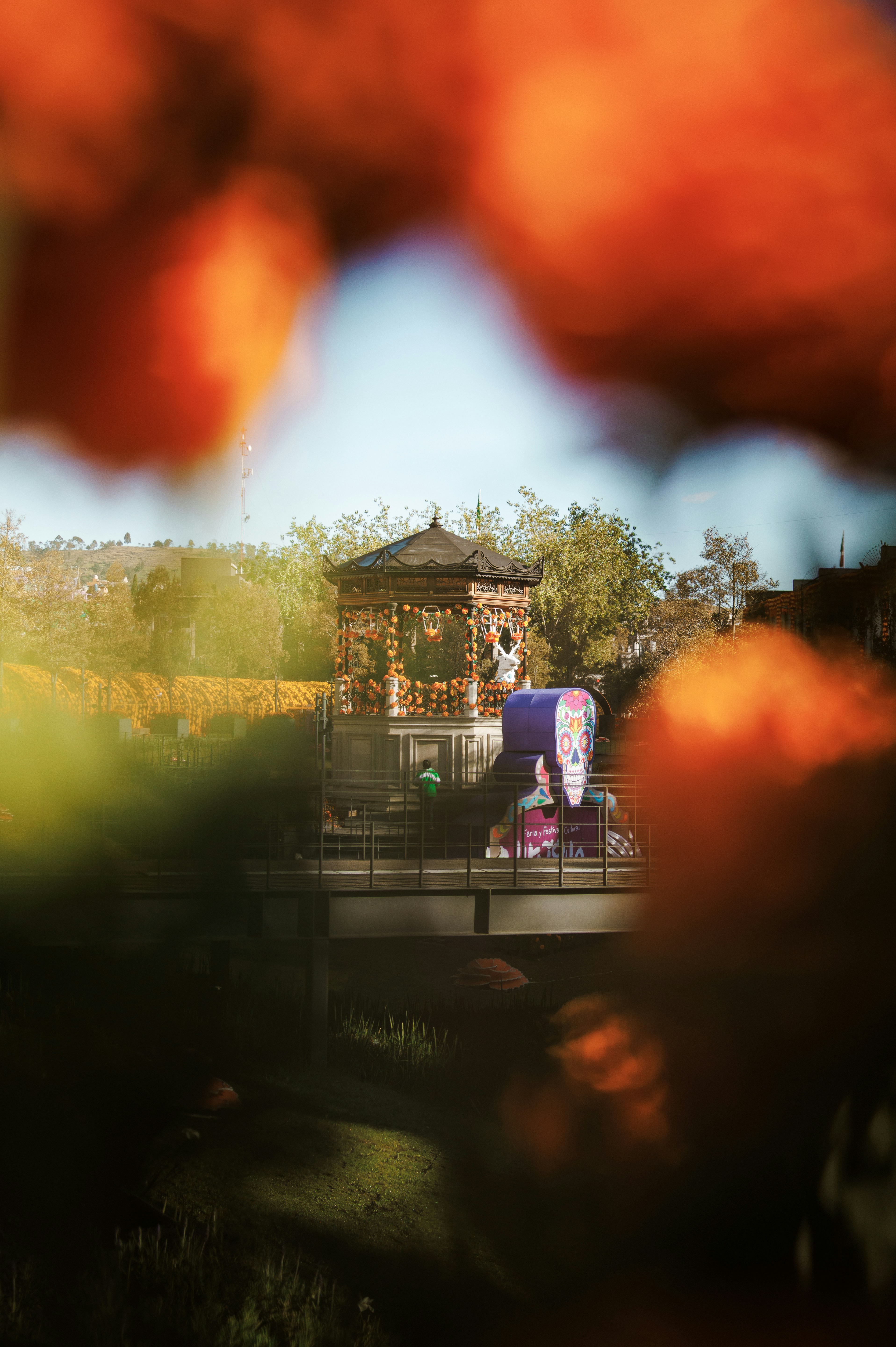 A gazebo decorated with orange marigolds and a skull cutout in a park
