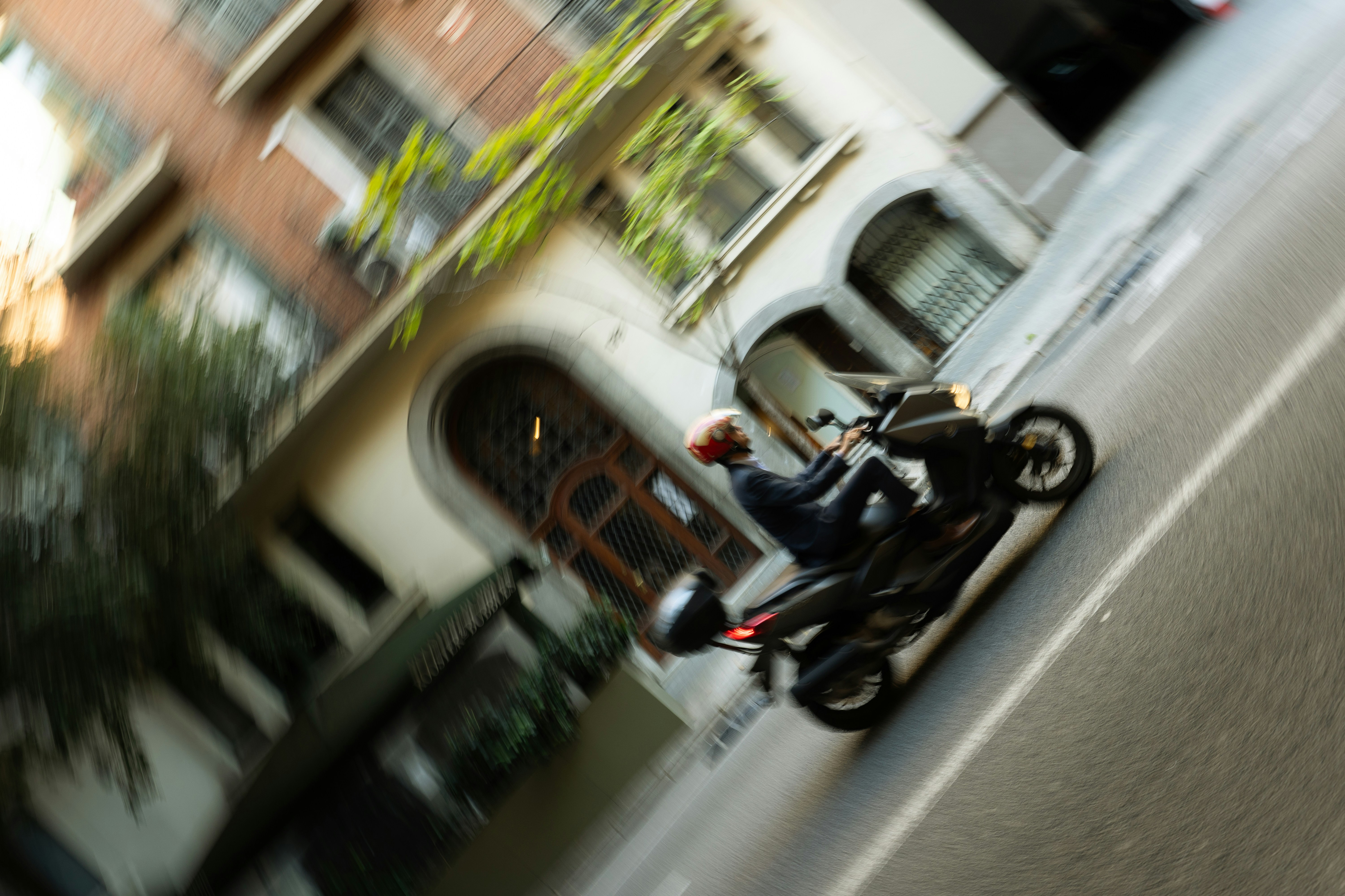 A person in a suit and helmet riding a scooter past a building in Barcelona