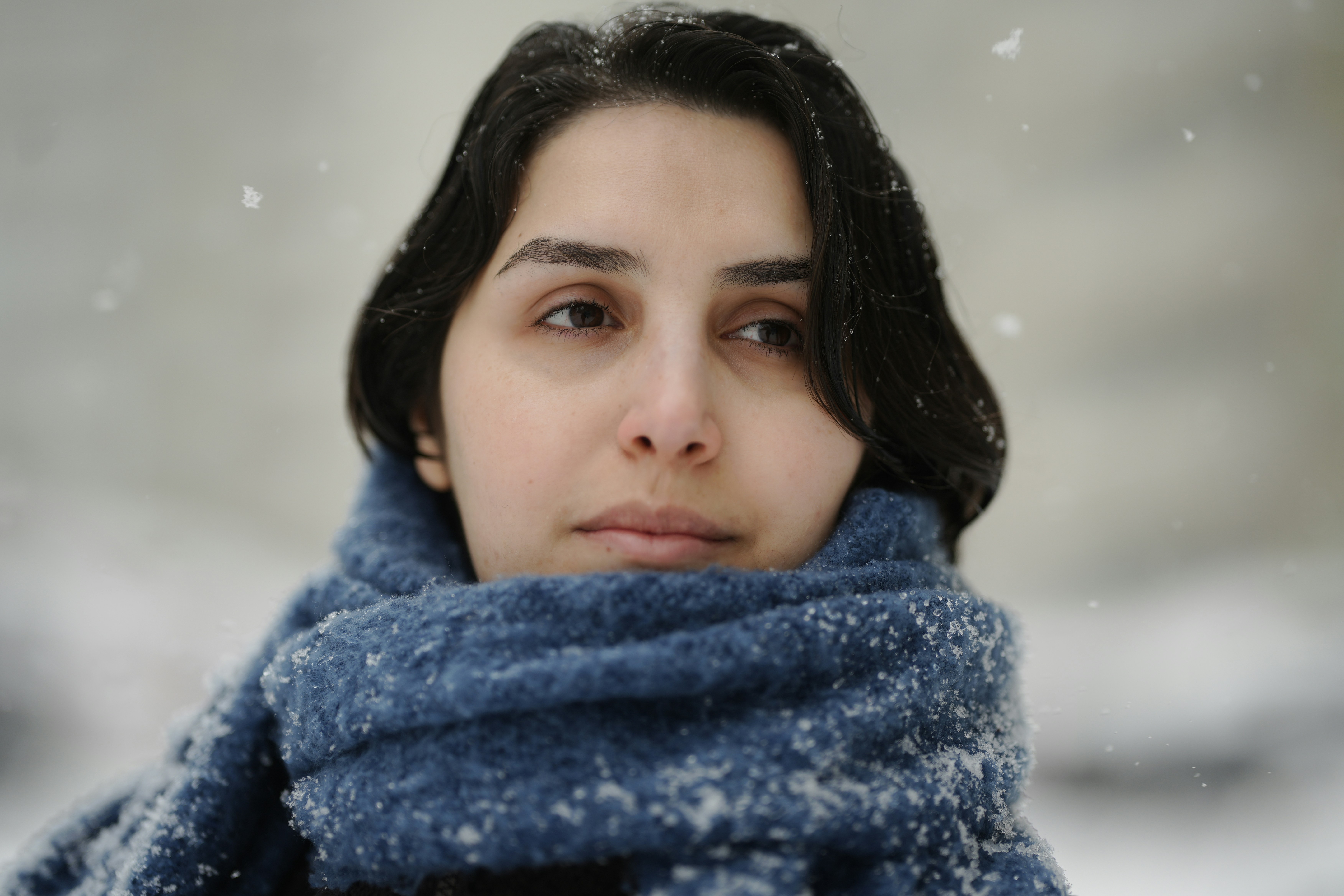 軽い雪の中で青いマフラーを巻いた黒髪の女性