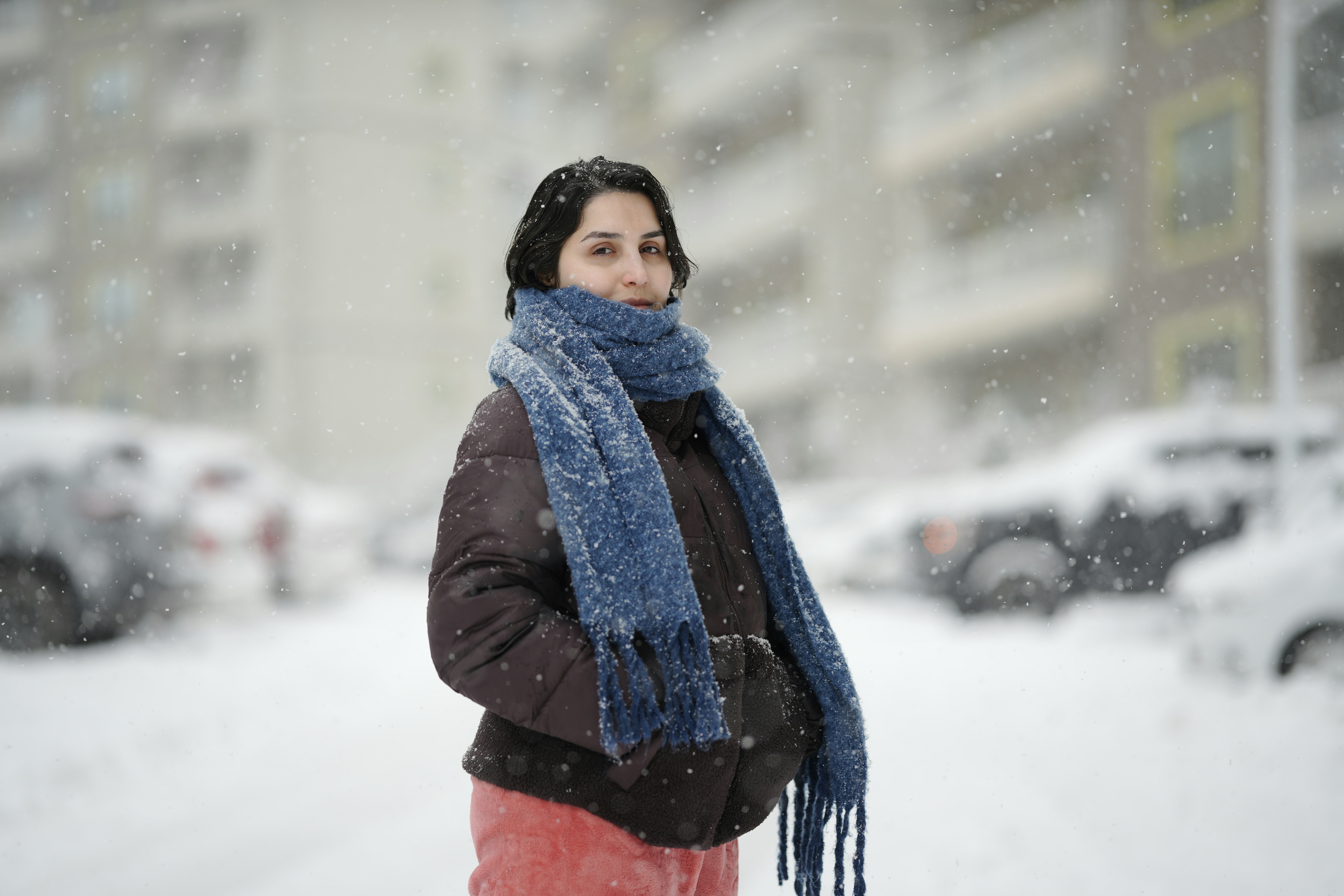 Uma mulher com jaqueta marrom e cachecol azul durante um dia de neve